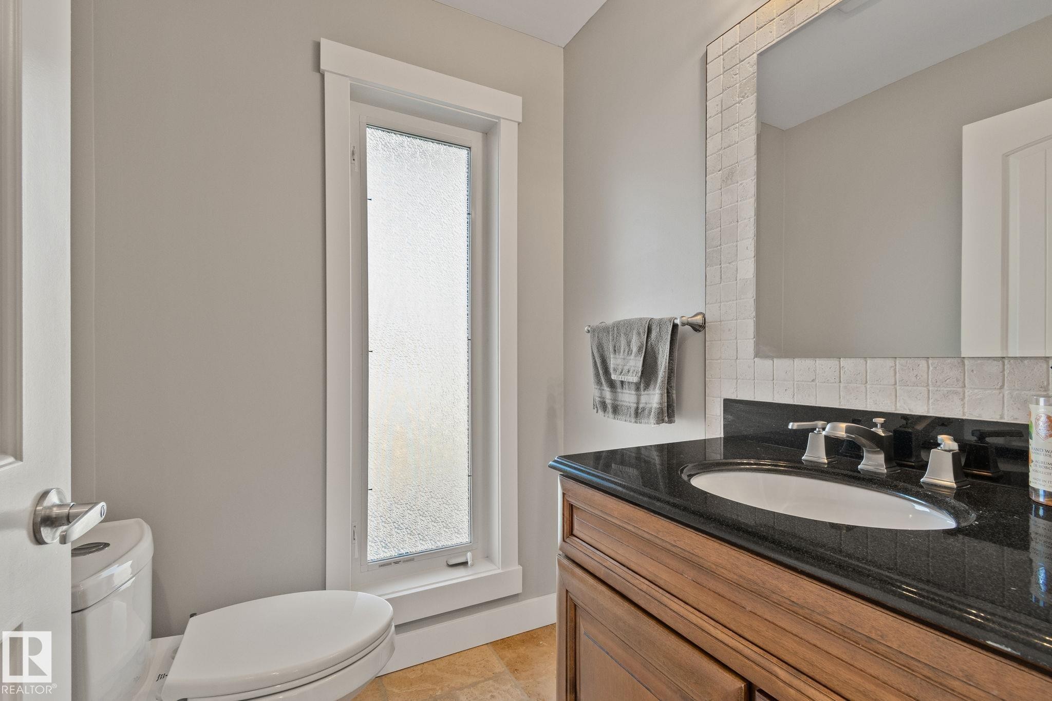 Wood-finish vanity with an undermount sink and dark countertop, complemented by a tile backsplash - 12403 29A Avenue Nw, Edmonton, AB