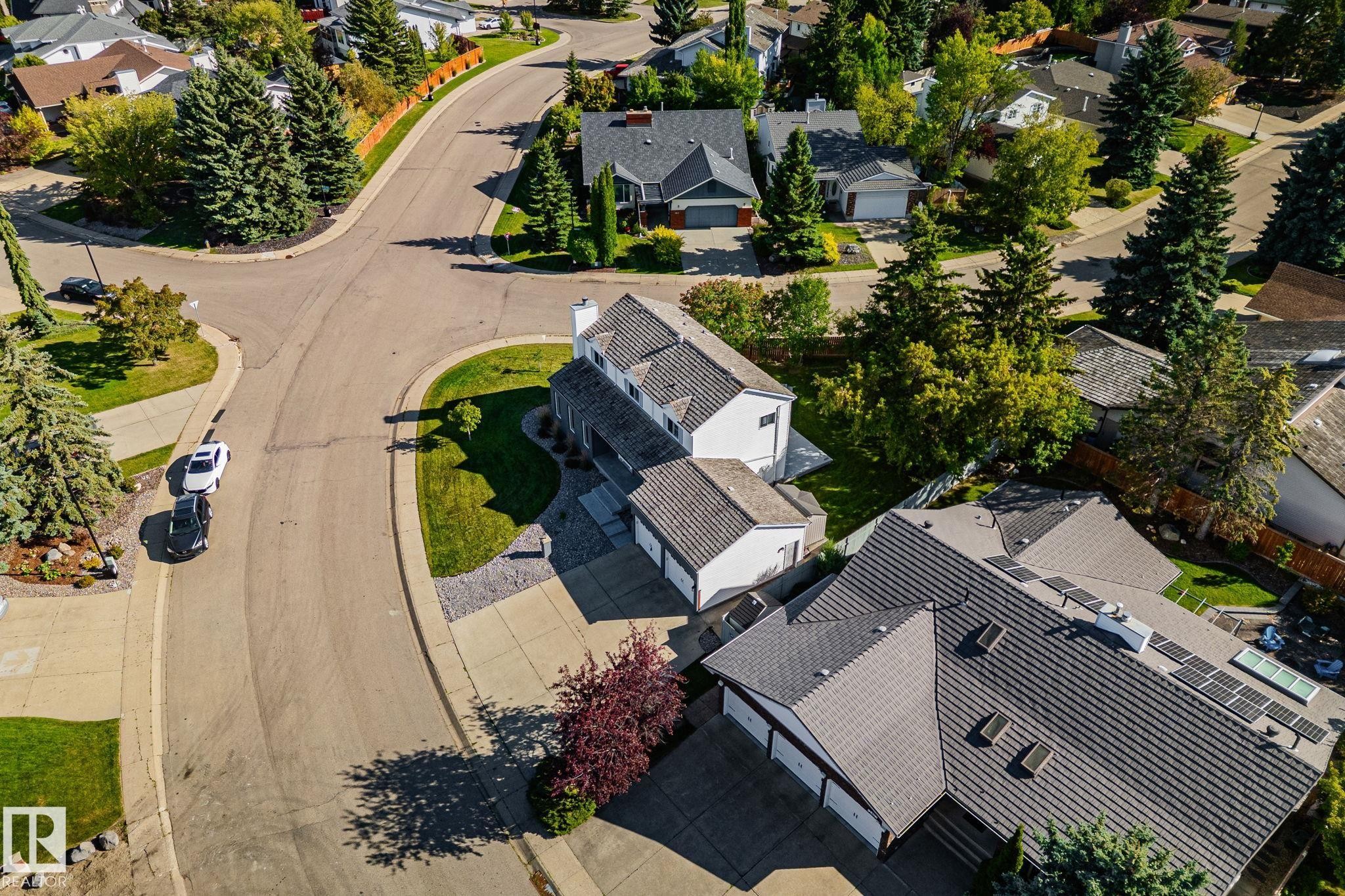 Paved roads winding through a residential area with mature landscaping, featuring a property with a multi-car garage, tiled roof, and integrated solar panels - 12403 29A Avenue Nw, Edmonton, AB