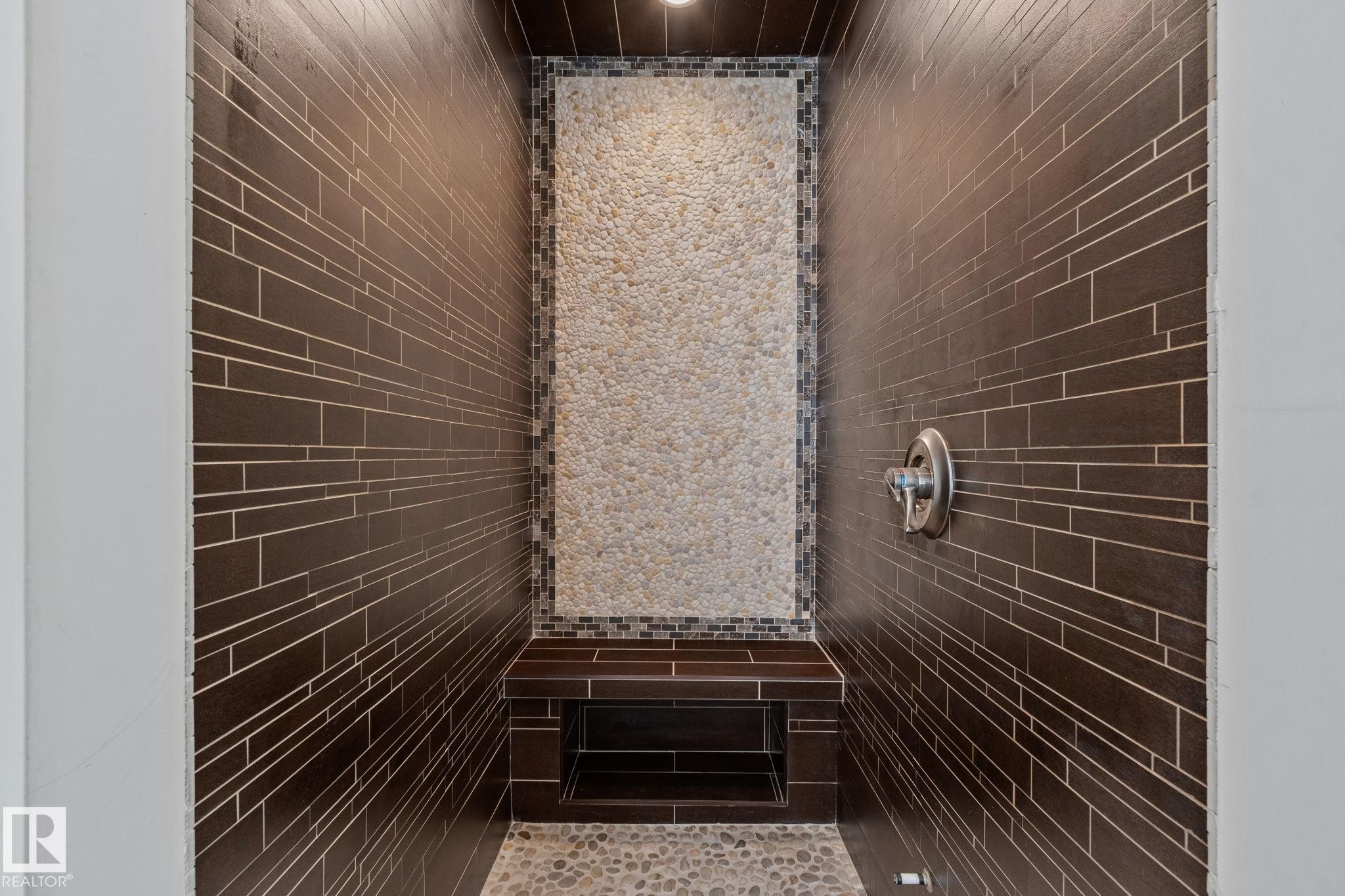 Walk-in shower with stone tile accent wall, built-in bench, recessed shelf, and pebble flooring - 12403 29A Avenue Nw, Edmonton, AB