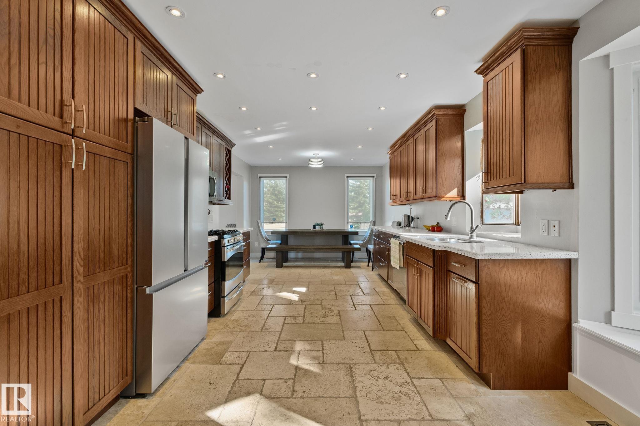 Kitchen featuring extensive wood cabinetry, stone tile flooring, recessed lighting, stainless steel appliances, and light-toned countertops - 12403 29A Avenue Nw, Edmonton, AB