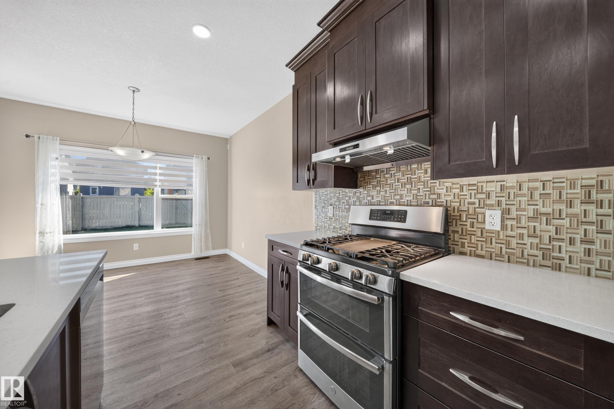 Expansive kitchen featuring dark wood cabinetry, white countertops, stainless steel range with hood, and a decorative tile backsplash - 121 64 Street Sw, Edmonton, AB