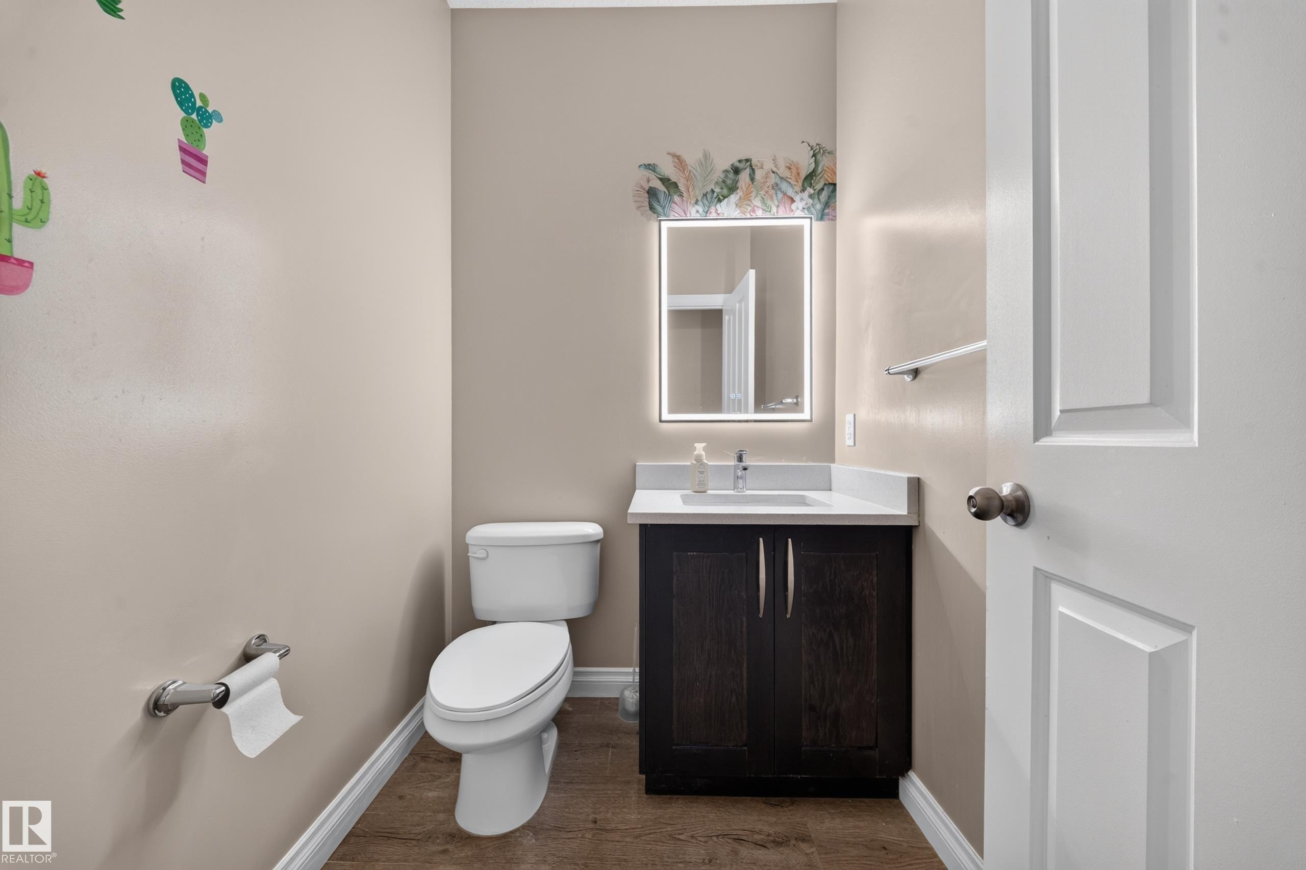 Powder room featuring a dark wood-finish vanity, white countertop with an integrated sink, and an illuminated mirror - 121 64 Street Sw, Edmonton, AB