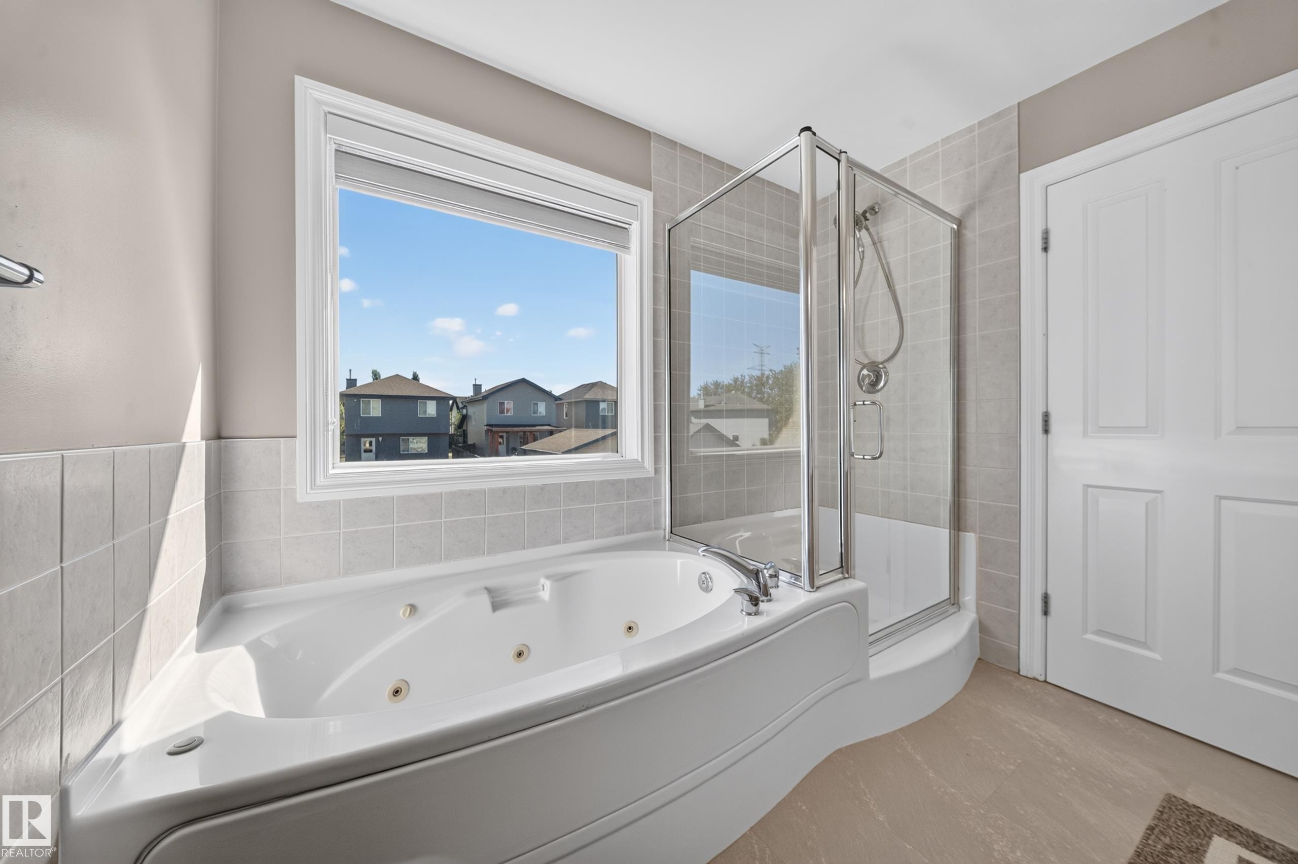 White paneled door, gray tiled shower with glass enclosure, white jetted tub, large window, and beige tile flooring - 121 64 Street Sw, Edmonton, AB