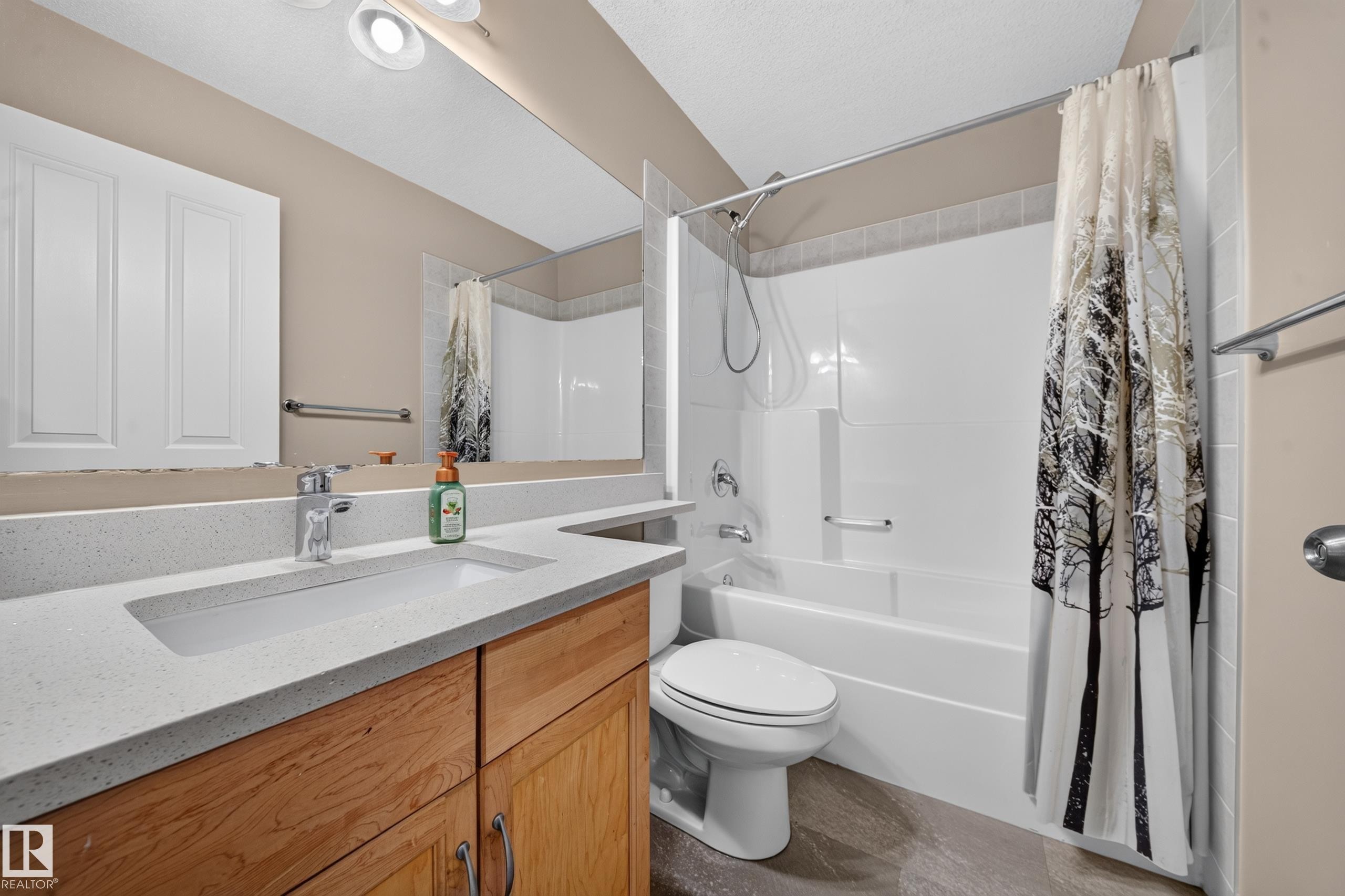 Bathroom featuring a wood-finish vanity with an integrated rectangular sink, light-toned countertop, and a shower-tub combination with white paneling - 121 64 Street Sw, Edmonton, AB