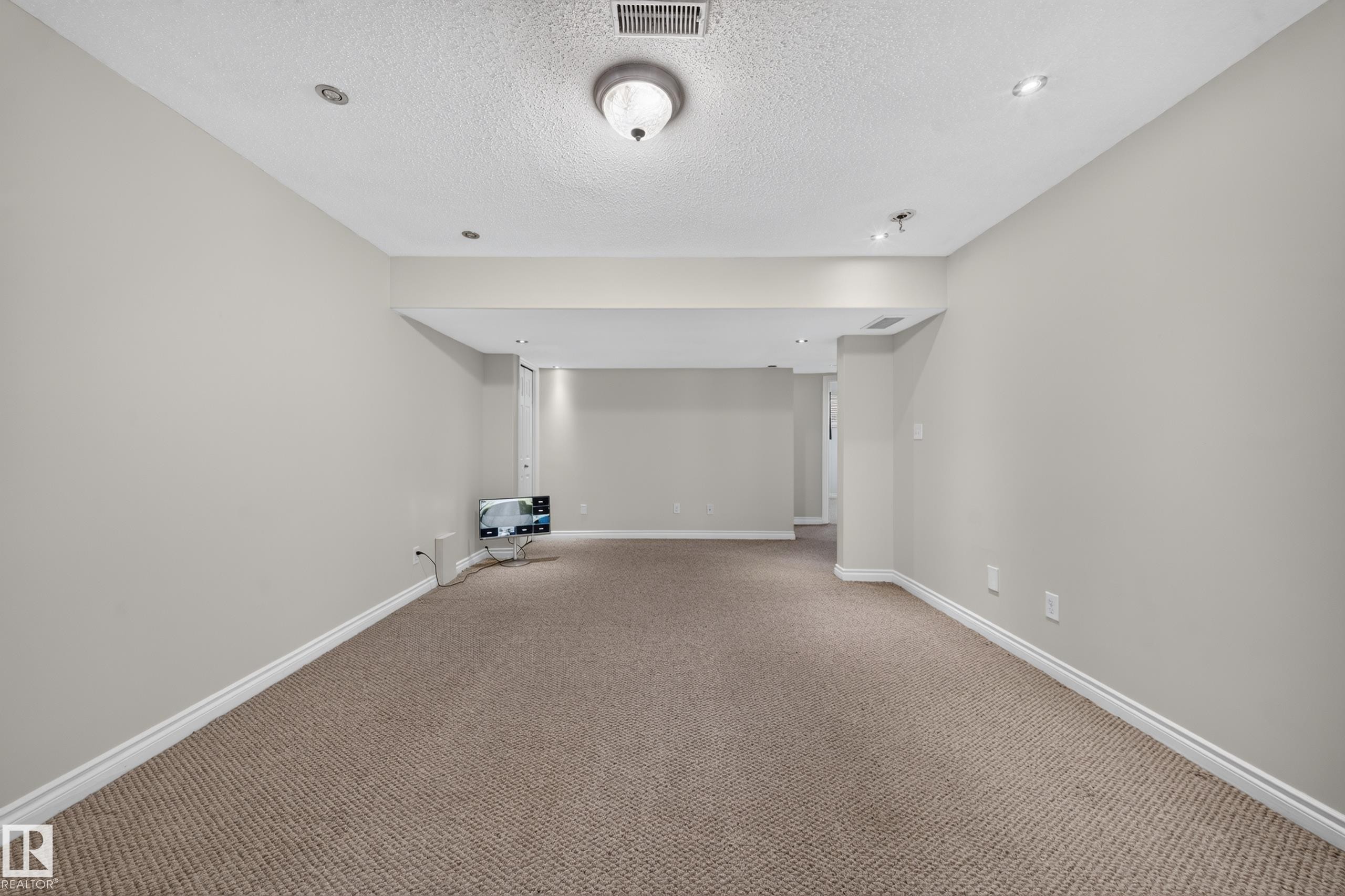 Spacious room featuring neutral carpeting, light gray wall paint, recessed lighting, and a drop ceiling with a central flush mount light fixture - 121 64 Street Sw, Edmonton, AB
