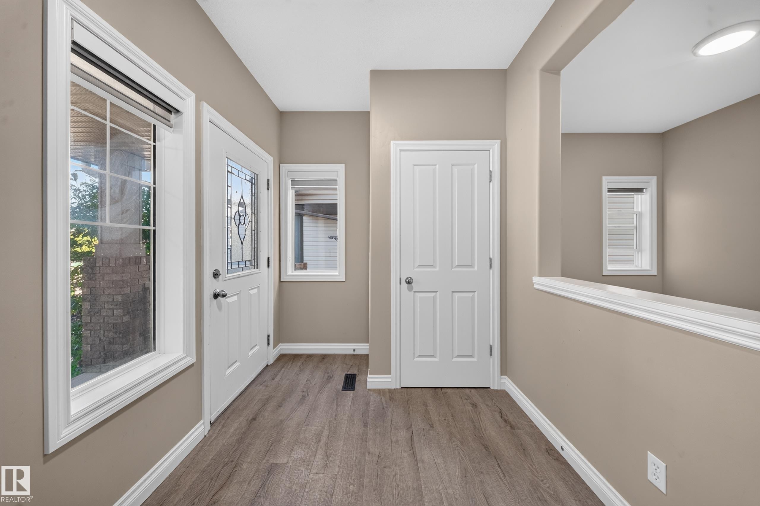 Entryway featuring wood-finish flooring, a white paneled door, a door with decorative glass, and a large window with grid panes - 121 64 Street Sw, Edmonton, AB