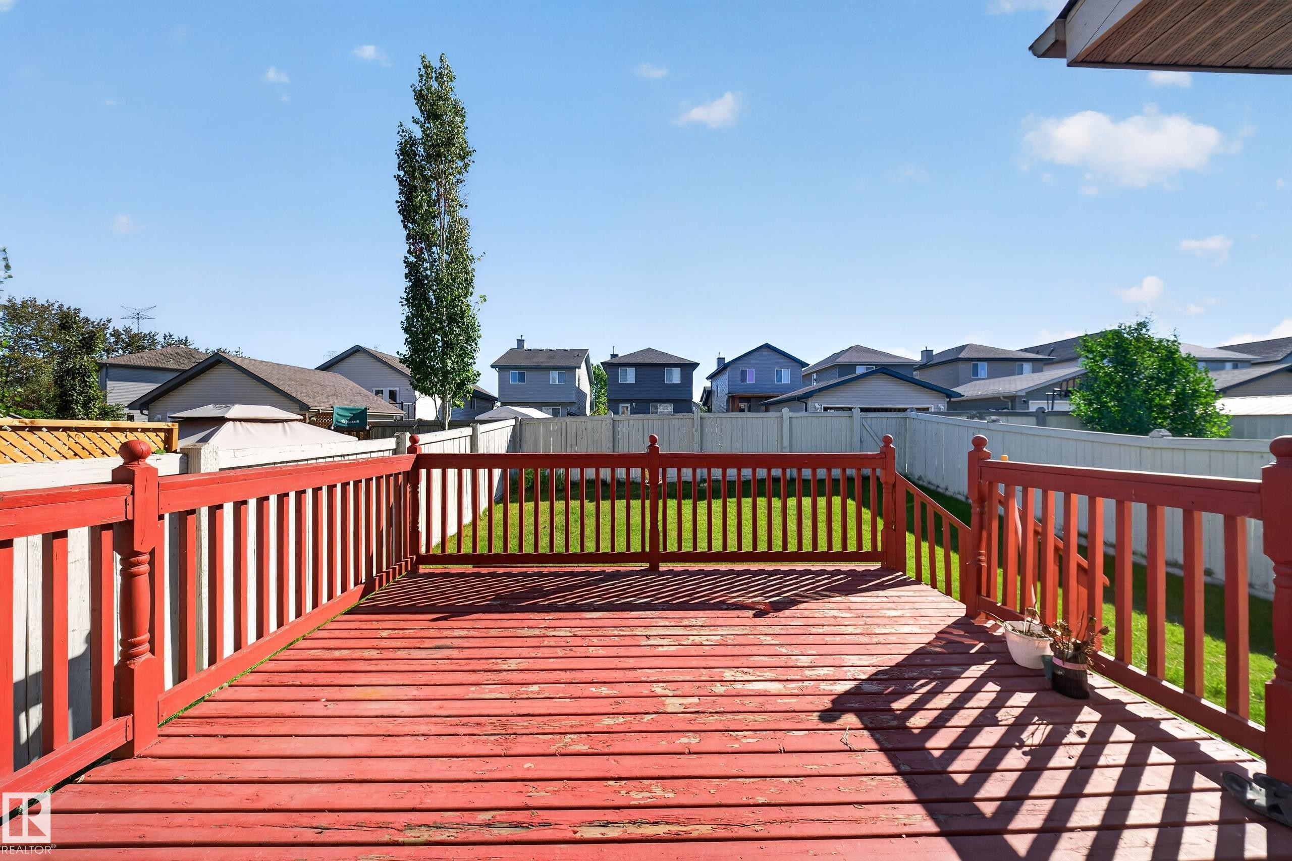 Expansive wood deck with red railings and stairs, overlooking a fenced backyard with a manicured lawn - 121 64 Street Sw, Edmonton, AB