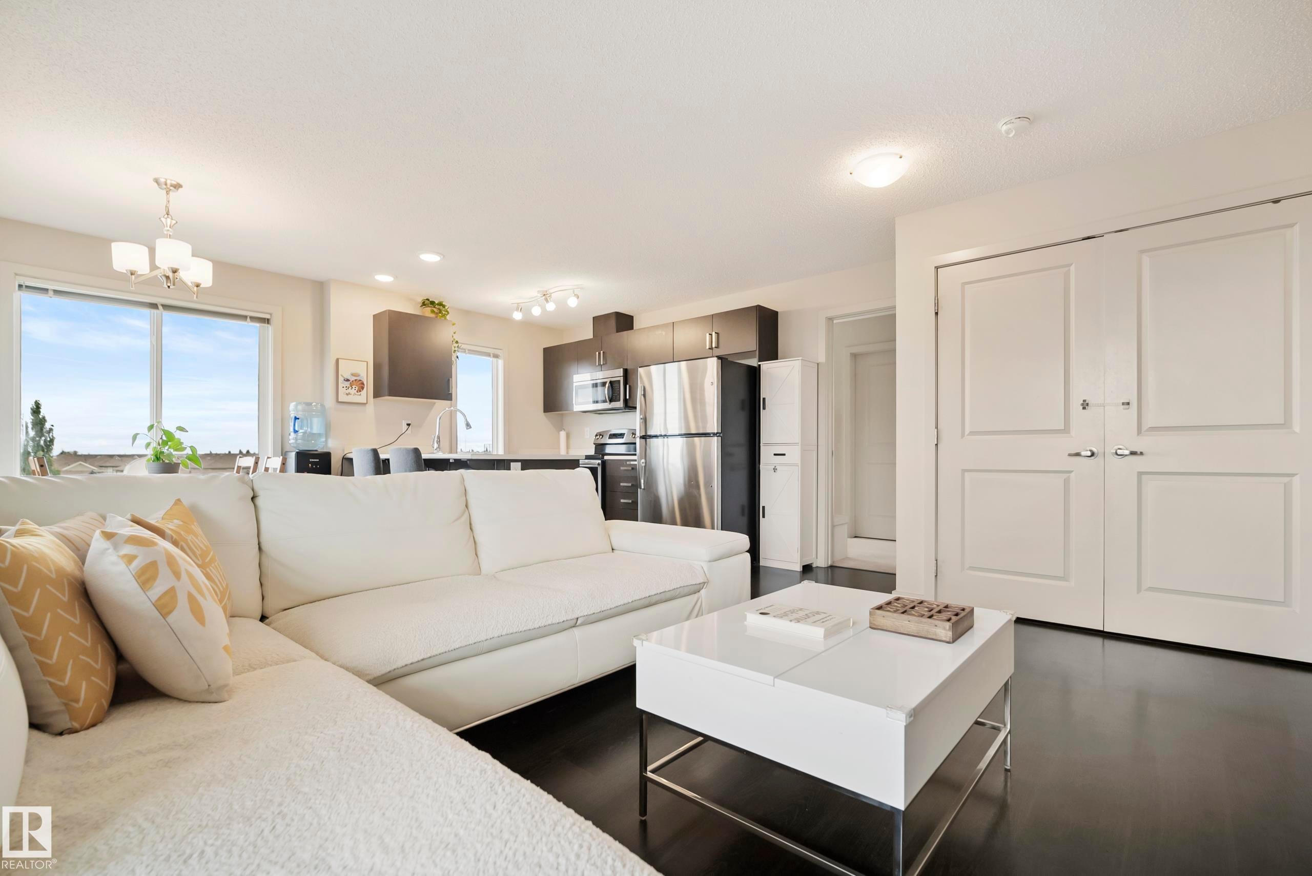 Expansive windows, dark wood-finish flooring, recessed lighting, double-panel bifold doors, and a contemporary kitchen with stainless steel appliances - #419 5515 7 Av Sw, Edmonton, AB