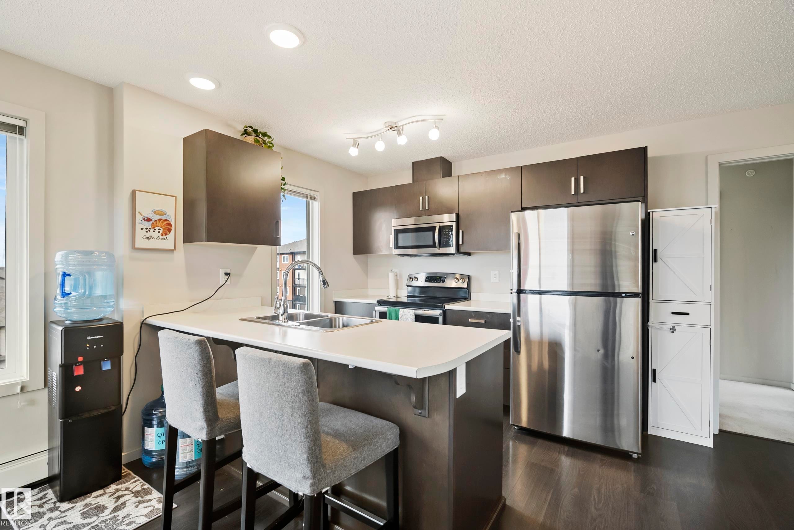 Kitchen with dark wood-finish cabinetry, stainless steel appliances, a center island with a sink, and recessed lighting - #419 5515 7 Av Sw, Edmonton, AB