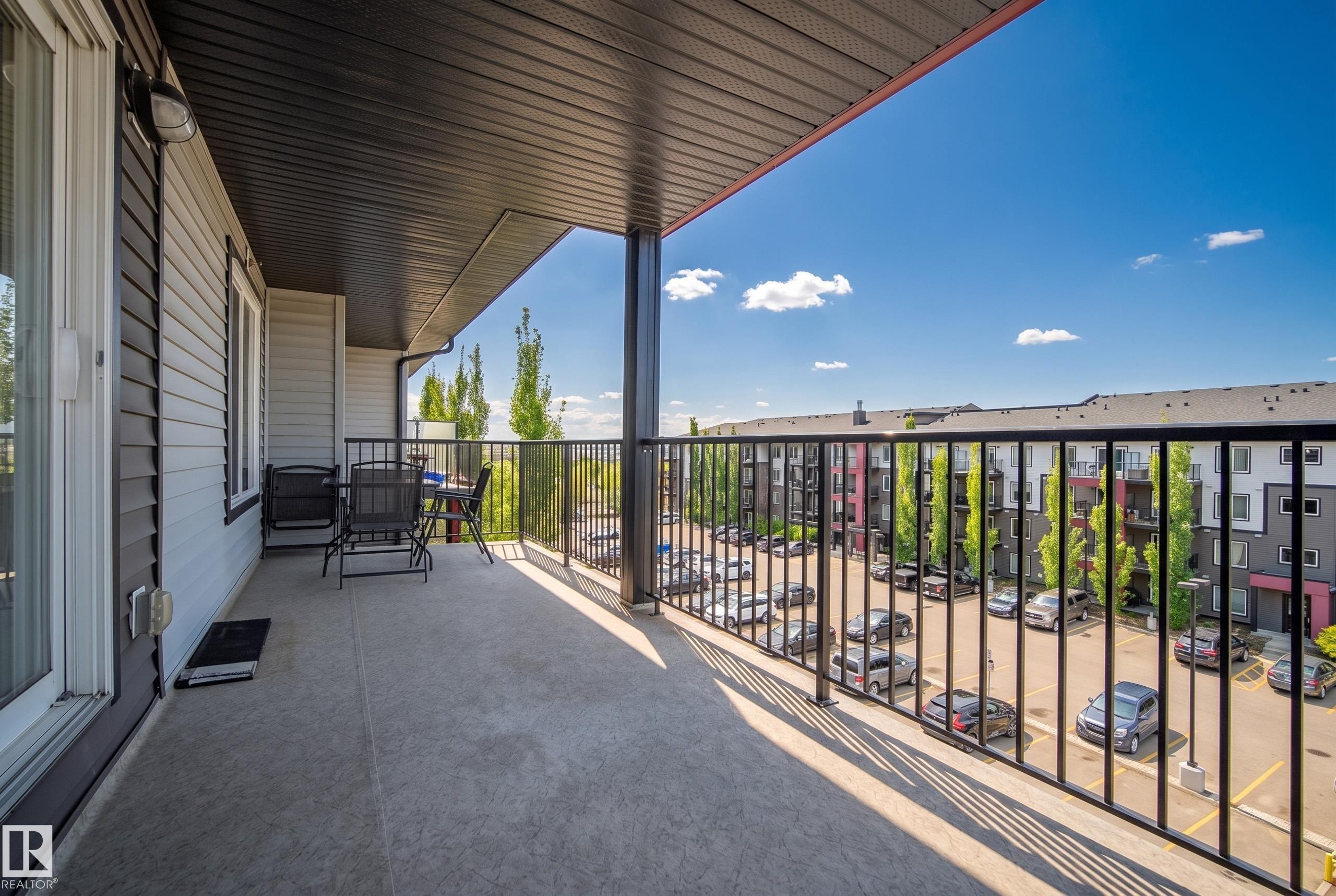 Spacious outdoor balcony with concrete flooring, black metal railings, and a dark soffit ceiling - #419 5515 7 Av Sw, Edmonton, AB