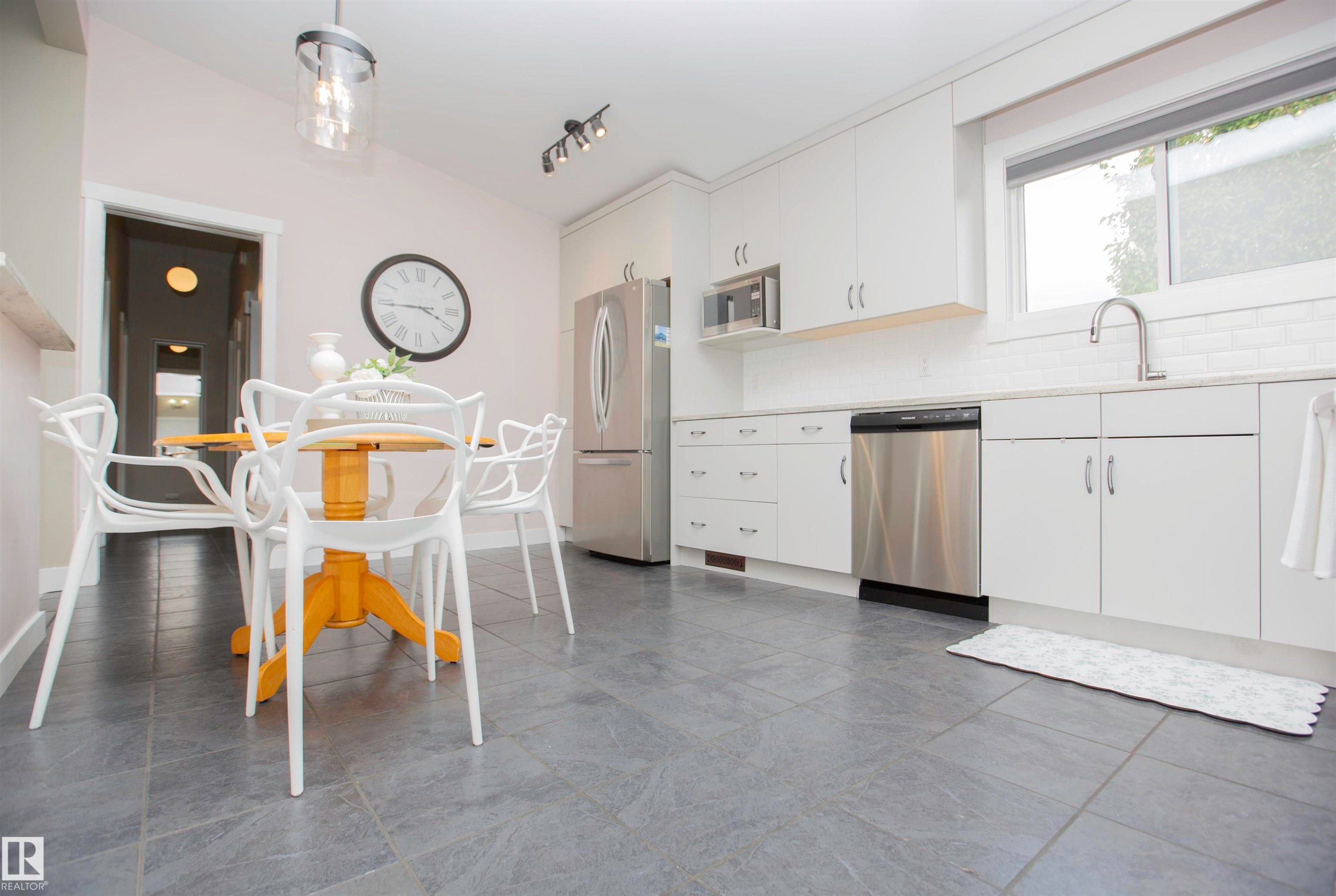 Kitchen featuring stone-look floor tiles, white shaker-style cabinetry, and stainless steel appliances - 9107 58 Street Nw, Edmonton, AB