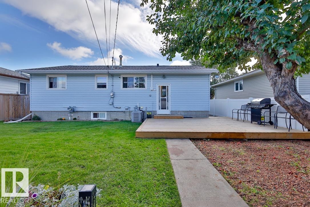 Expansive rear yard featuring a wooden deck, a concrete pathway, and a mature tree - 13312 123A Street Nw, Edmonton, AB
