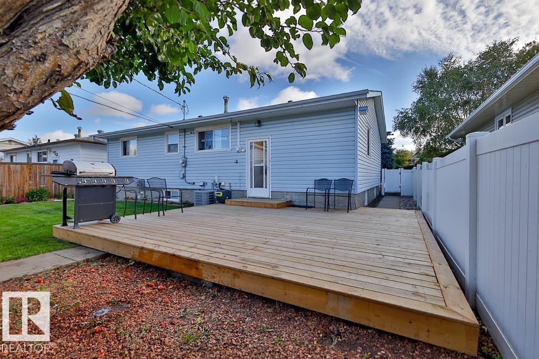 Expansive wood deck with direct access to the interior, featuring light blue siding, a manicured lawn, and a white privacy fence - 13312 123A Street Nw, Edmonton, AB