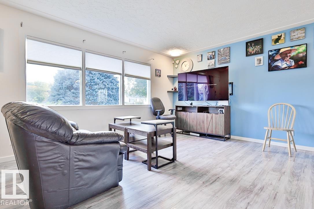 Light wood-finish flooring, accent wall, built-in shelving, and multiple windows with shades - 13312 123A Street Nw, Edmonton, AB
