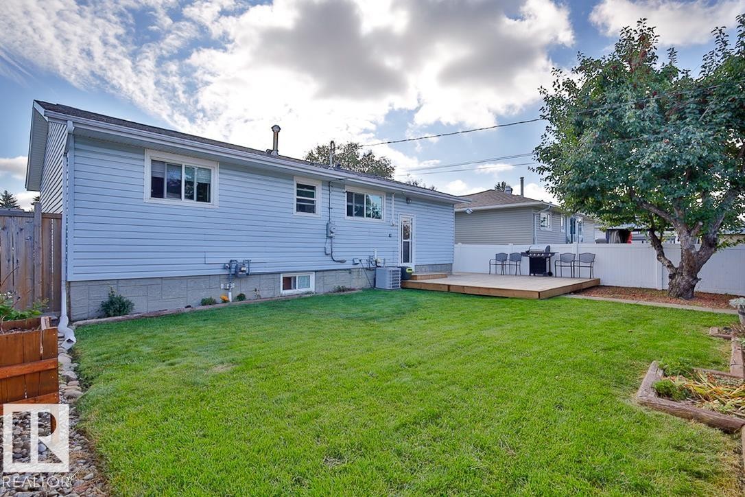 Expansive backyard featuring a manicured lawn, a raised wooden deck, a mature tree, and a white privacy fence - 13312 123A Street Nw, Edmonton, AB