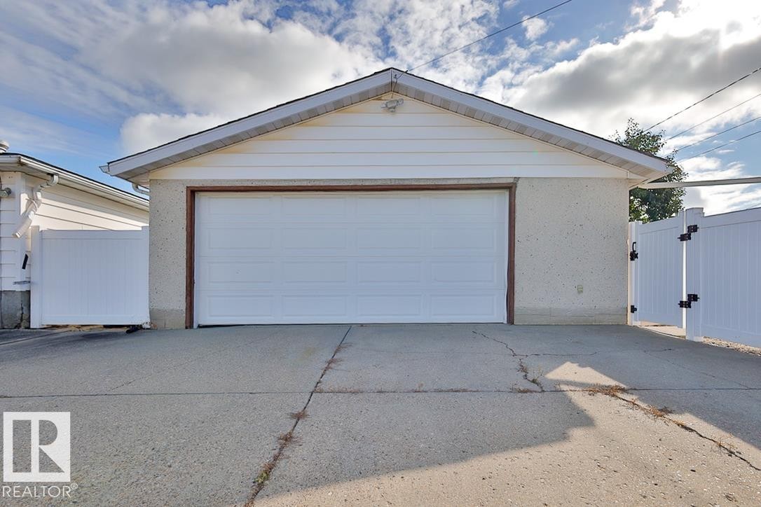 Detached garage with a white panel door, light-colored siding, and a gabled roofline - 13312 123A Street Nw, Edmonton, AB