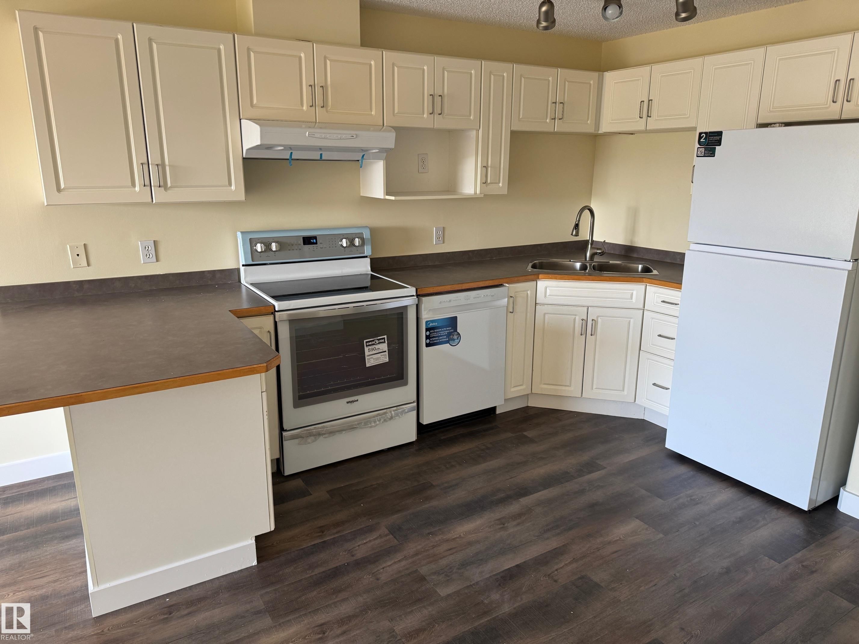Kitchen with wood-finish flooring, white cabinetry, dark countertops, white appliances, and track lighting - #229 2305 35A Av Nw, Edmonton, AB