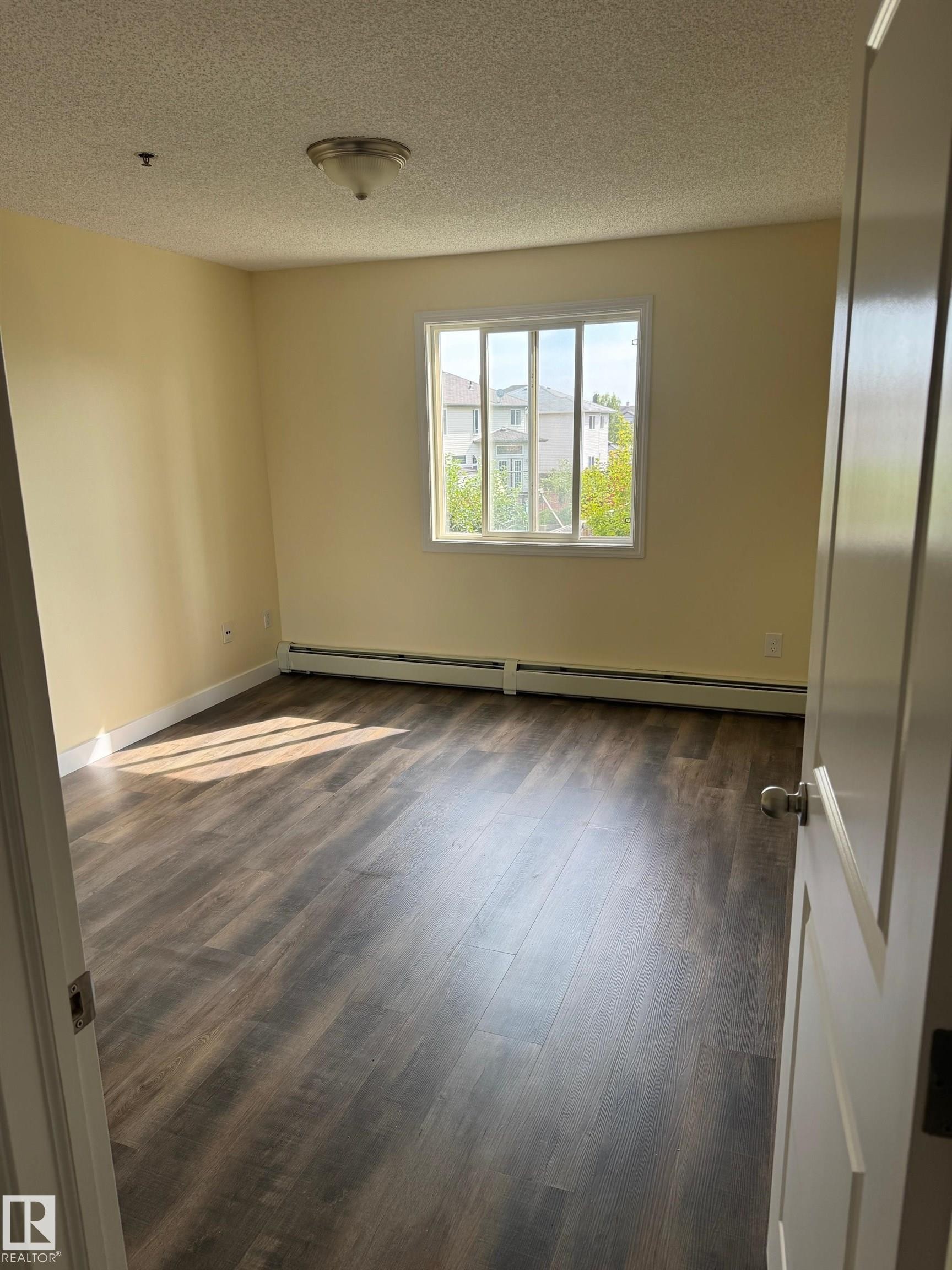 Wood-finish flooring with a smooth texture, bright white trim, and a ceiling-mounted light fixture - #229 2305 35A Av Nw, Edmonton, AB