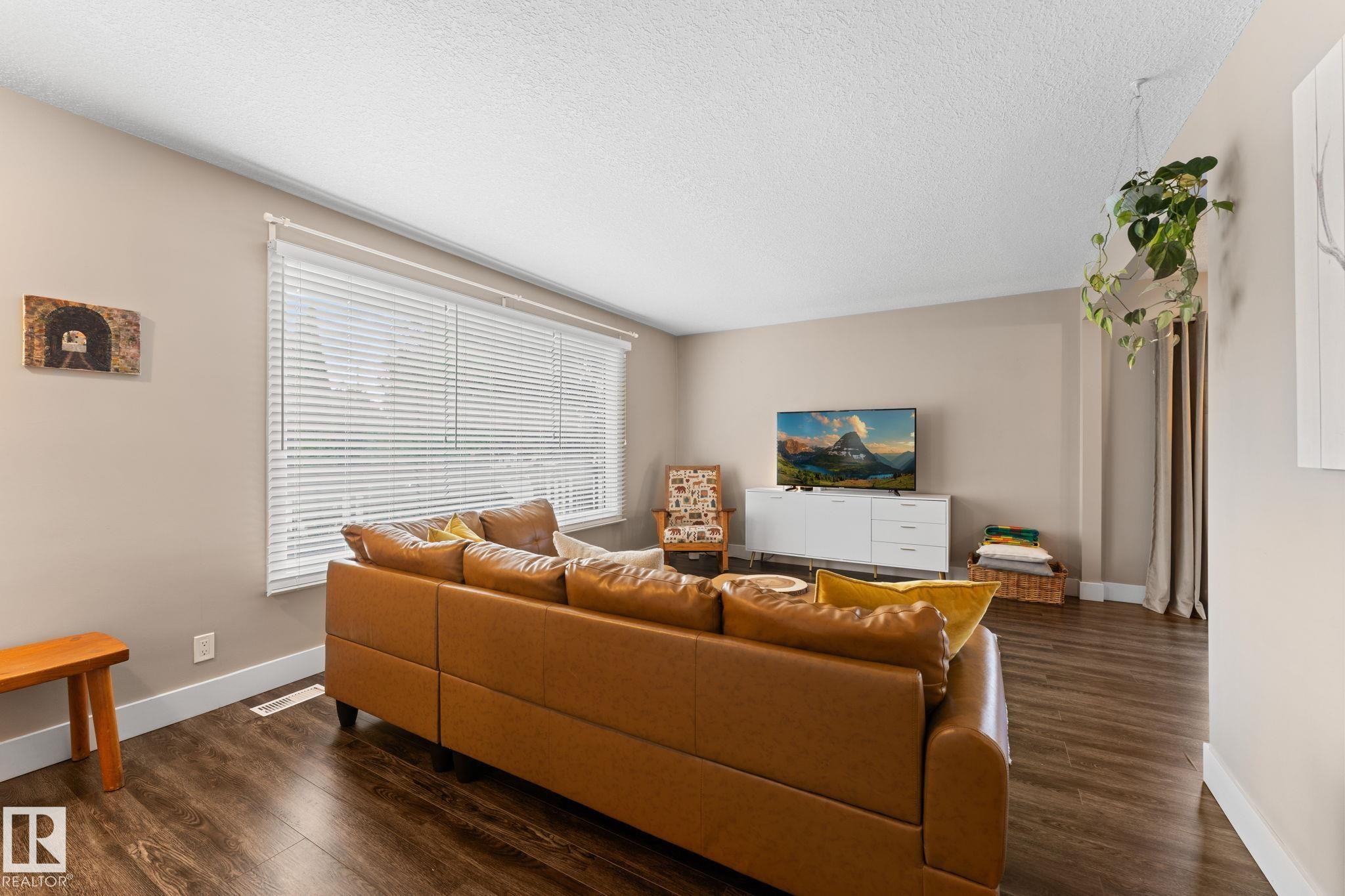 Spacious room featuring lamanite flooring, neutral paint, a large window with blinds, and white trim - 6108 102 Avenue Nw, Edmonton, AB