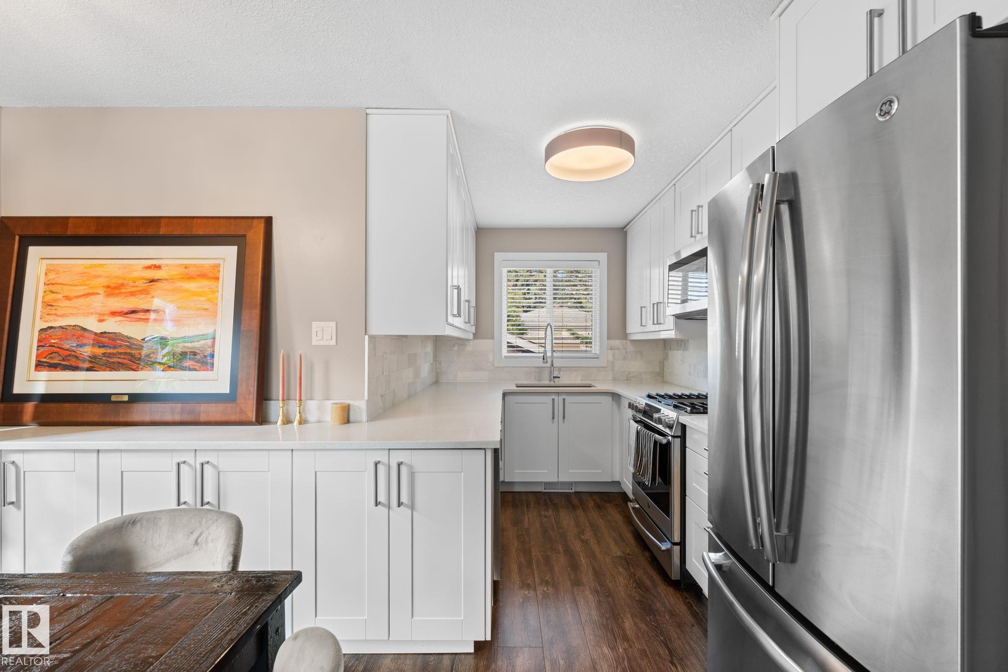 White shaker cabinetry, stainless steel appliances, laminate flooring, white countertops, and a subway tile backsplash - 6108 102 Avenue Nw, Edmonton, AB