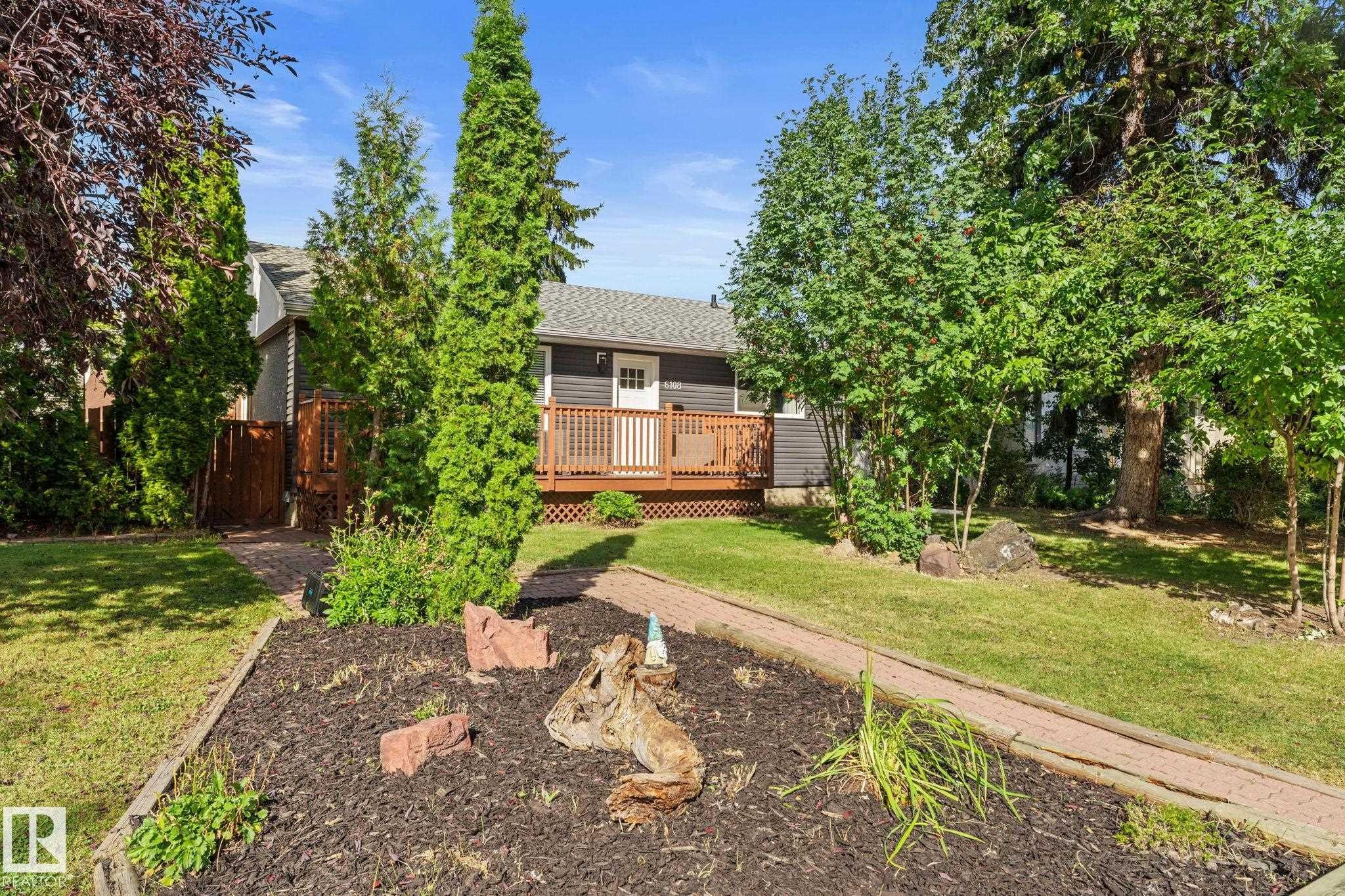 Exterior featuring a wood deck, dark gray siding, and a white entrance door - 6108 102 Avenue Nw, Edmonton, AB
