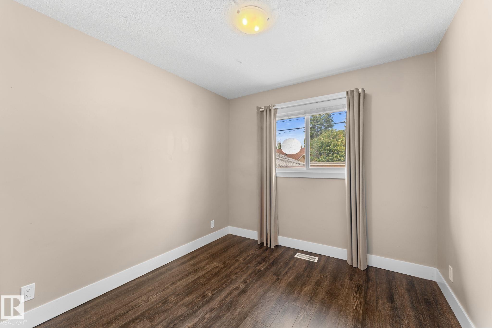 Laminate flooring, neutral wall tones, white trim, window with natural light, and ceiling-mounted light fixture - 6108 102 Avenue Nw, Edmonton, AB