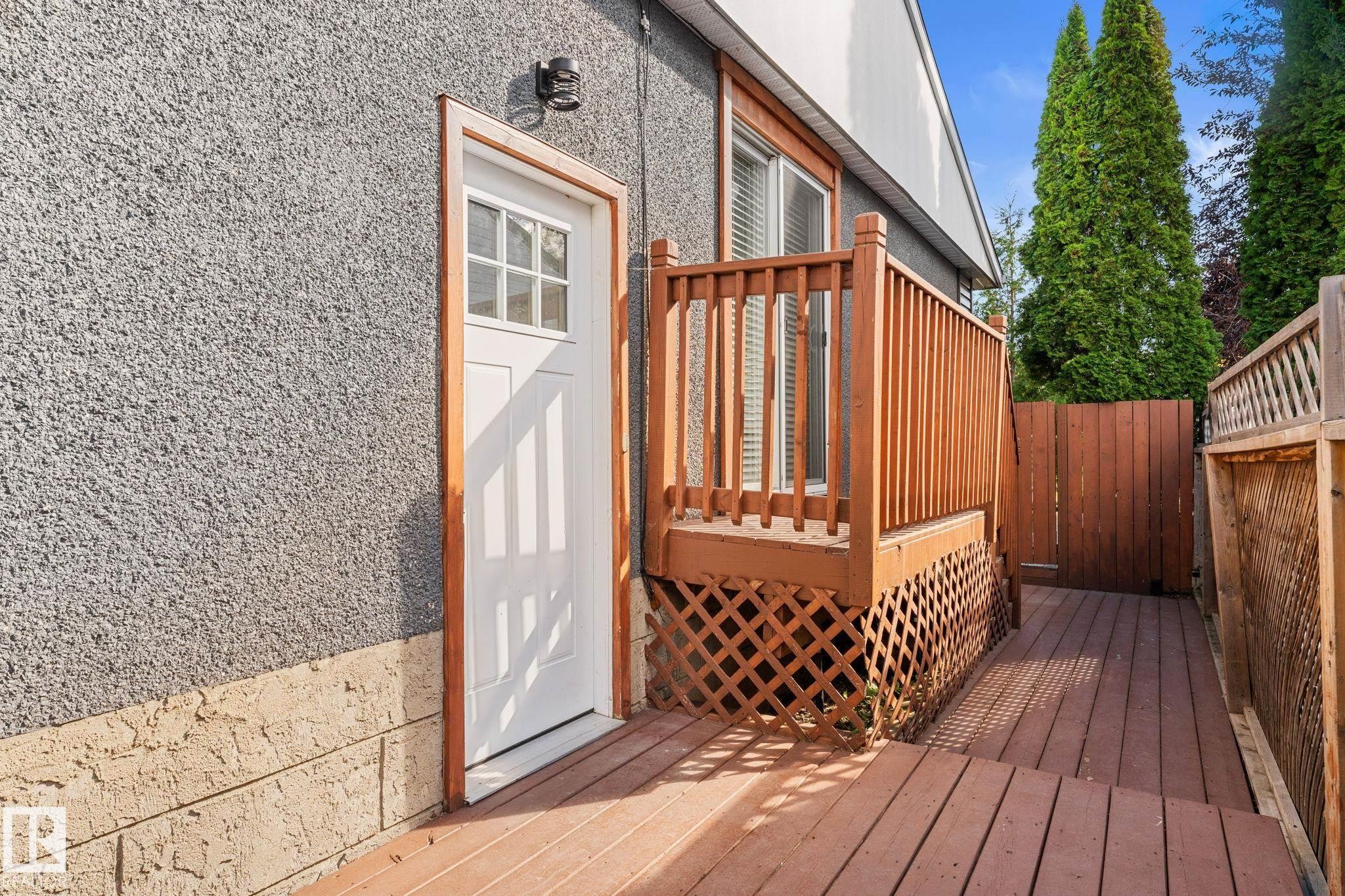 Wood-finish deck with privacy fencing, lattice skirting, and a transom-style entry door for the basement suite - 6108 102 Avenue Nw, Edmonton, AB