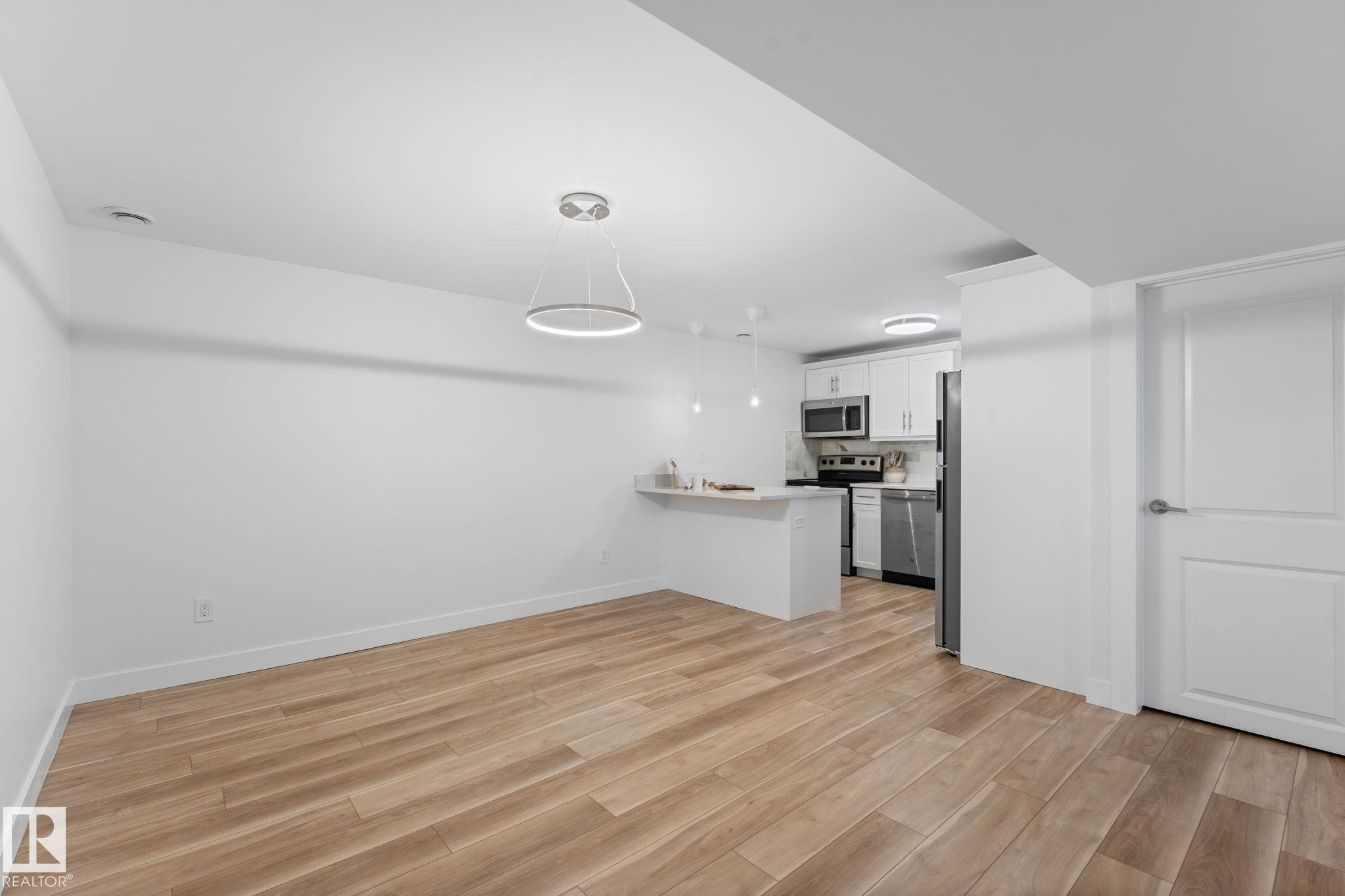 Open-concept dining area with vinyl plank flooring, white walls, and a contemporary ceiling light fixture - 6108 102 Avenue Nw, Edmonton, AB