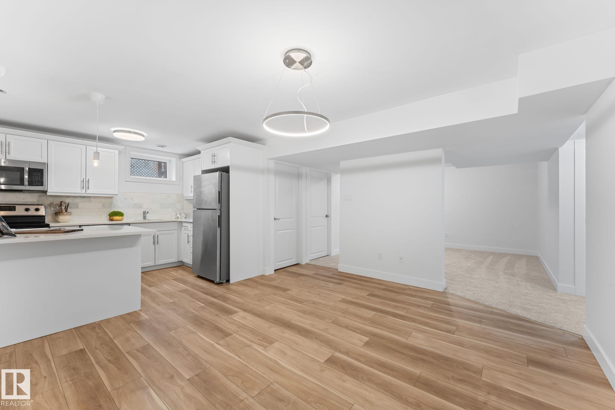 Open-concept dining and kitchen area with vinyl plank flooring, white walls, white cabinetry, stainless steel appliances, and a contemporary ceiling light fixture - 6108 102 Avenue Nw, Edmonton, AB