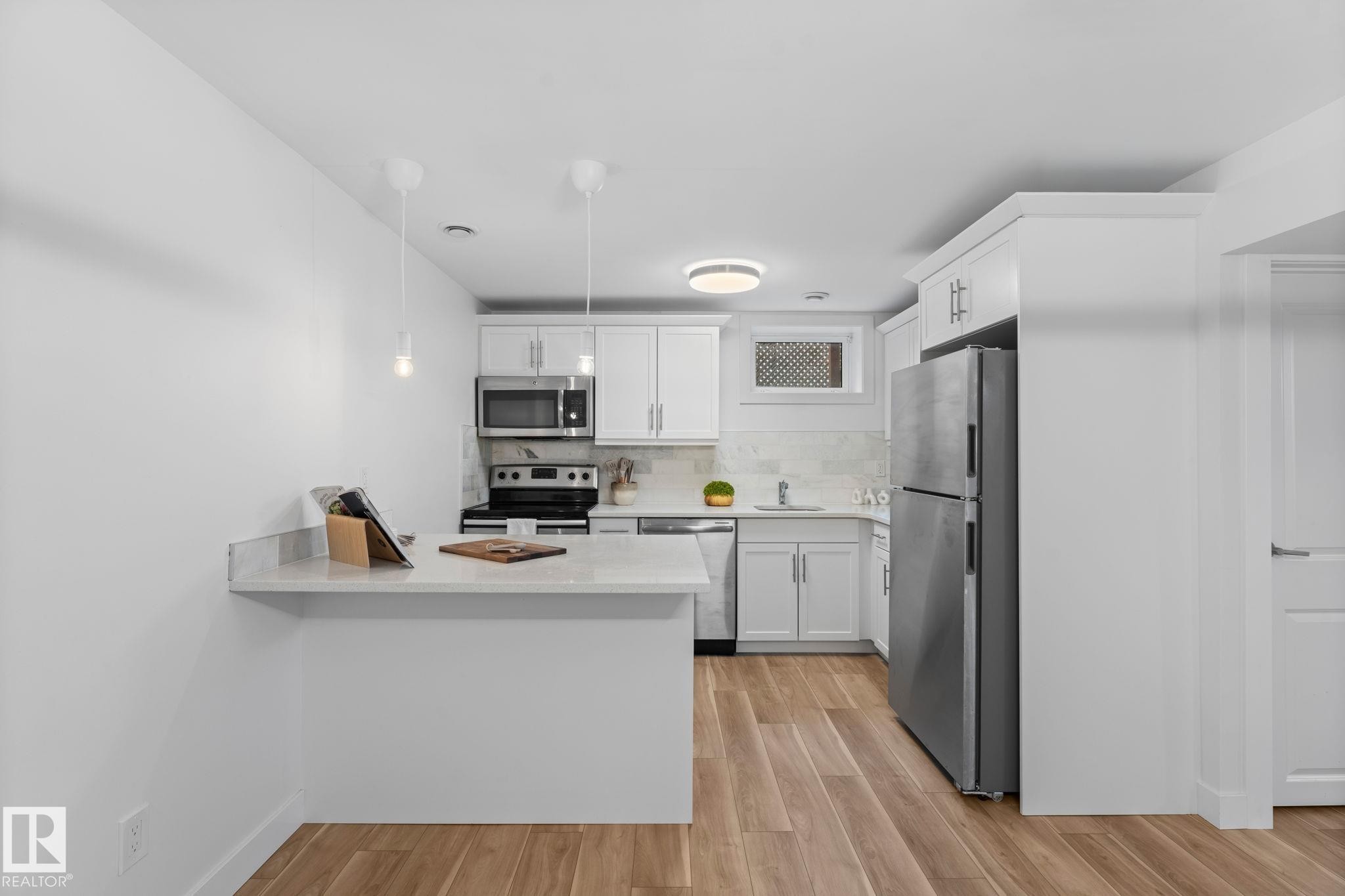 Kitchen featuring vinyl plank flooring, white cabinetry, stainless steel appliances, and a light-toned quartz countertop with a breakfast bar - 6108 102 Avenue Nw, Edmonton, AB