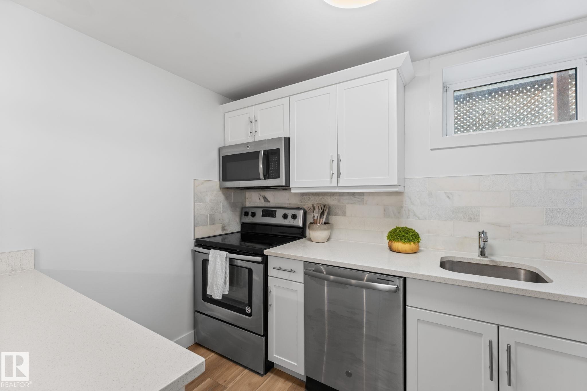 Kitchen featuring vinyl plank flooring, white cabinetry, stainless steel appliances, and a light-toned quartz countertop with a breakfast bar - 6108 102 Avenue Nw, Edmonton, AB