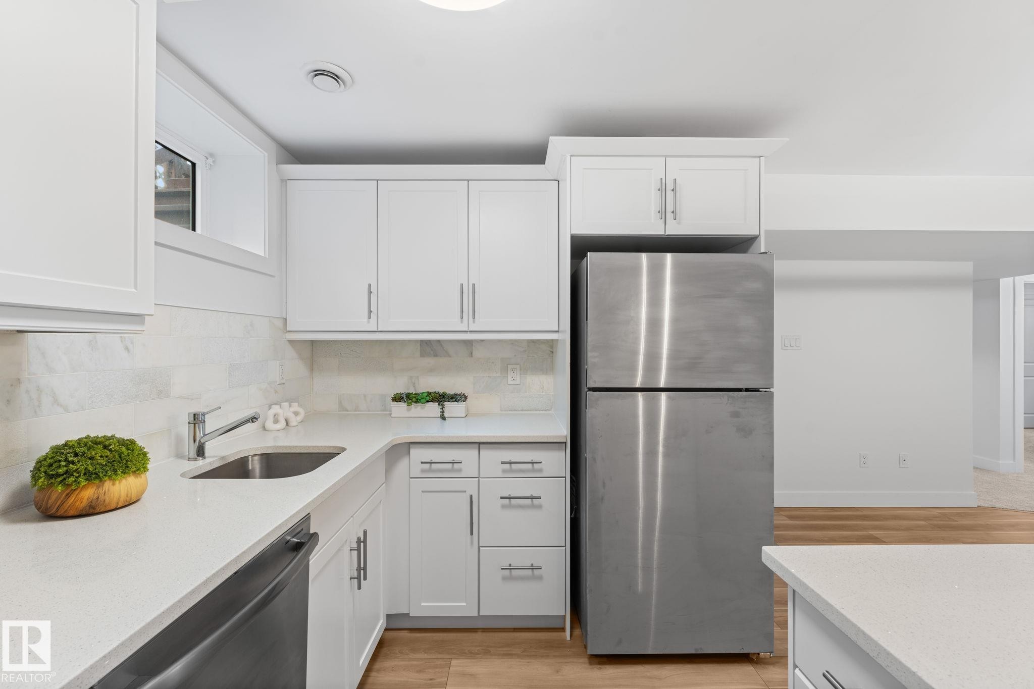Kitchen featuring vinyl plank flooring, white cabinetry, stainless steel appliances, and a light-toned quartz countertop with a breakfast bar - 6108 102 Avenue Nw, Edmonton, AB