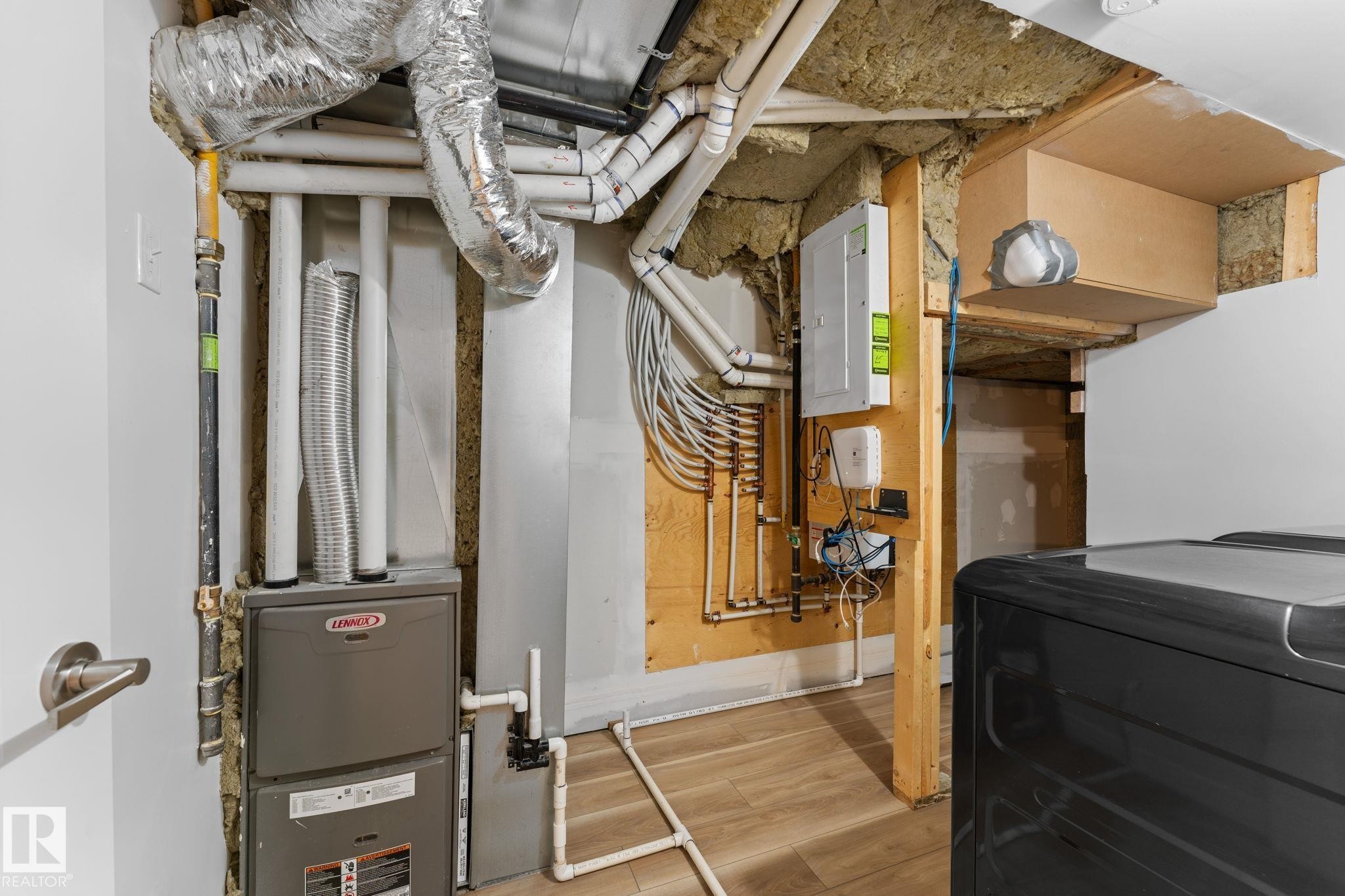 Utility area featuring upstairs furnace, ductwork, exposed insulation, wood-finish flooring, and an electrical panel - 6108 102 Avenue Nw, Edmonton, AB