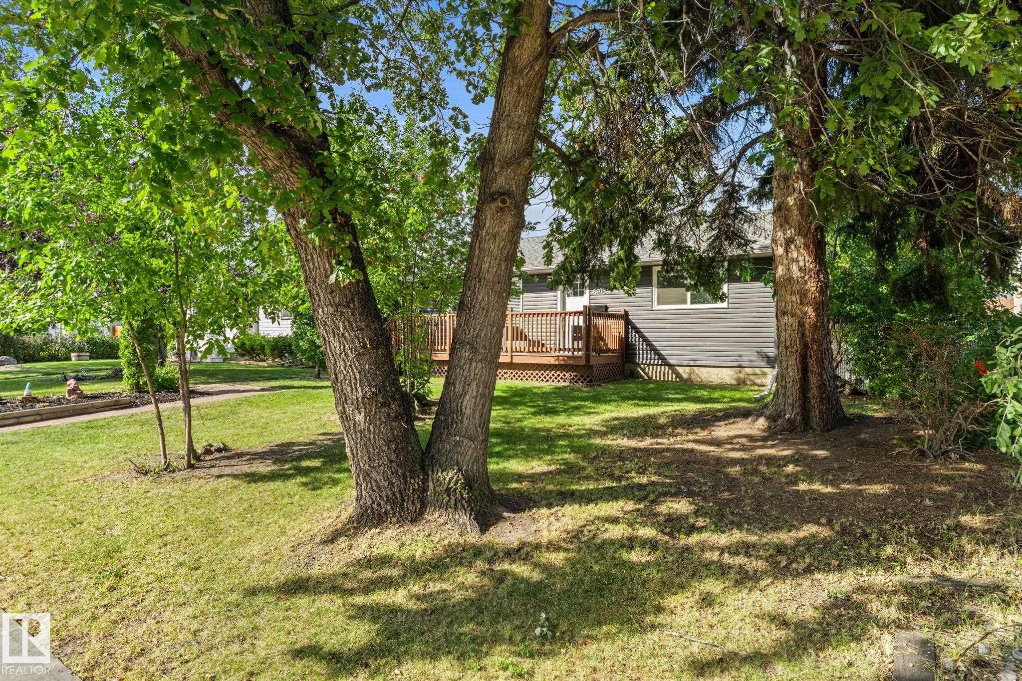 Exterior featuring a wood deck, dark gray siding, and a white entrance door - 6108 102 Avenue Nw, Edmonton, AB