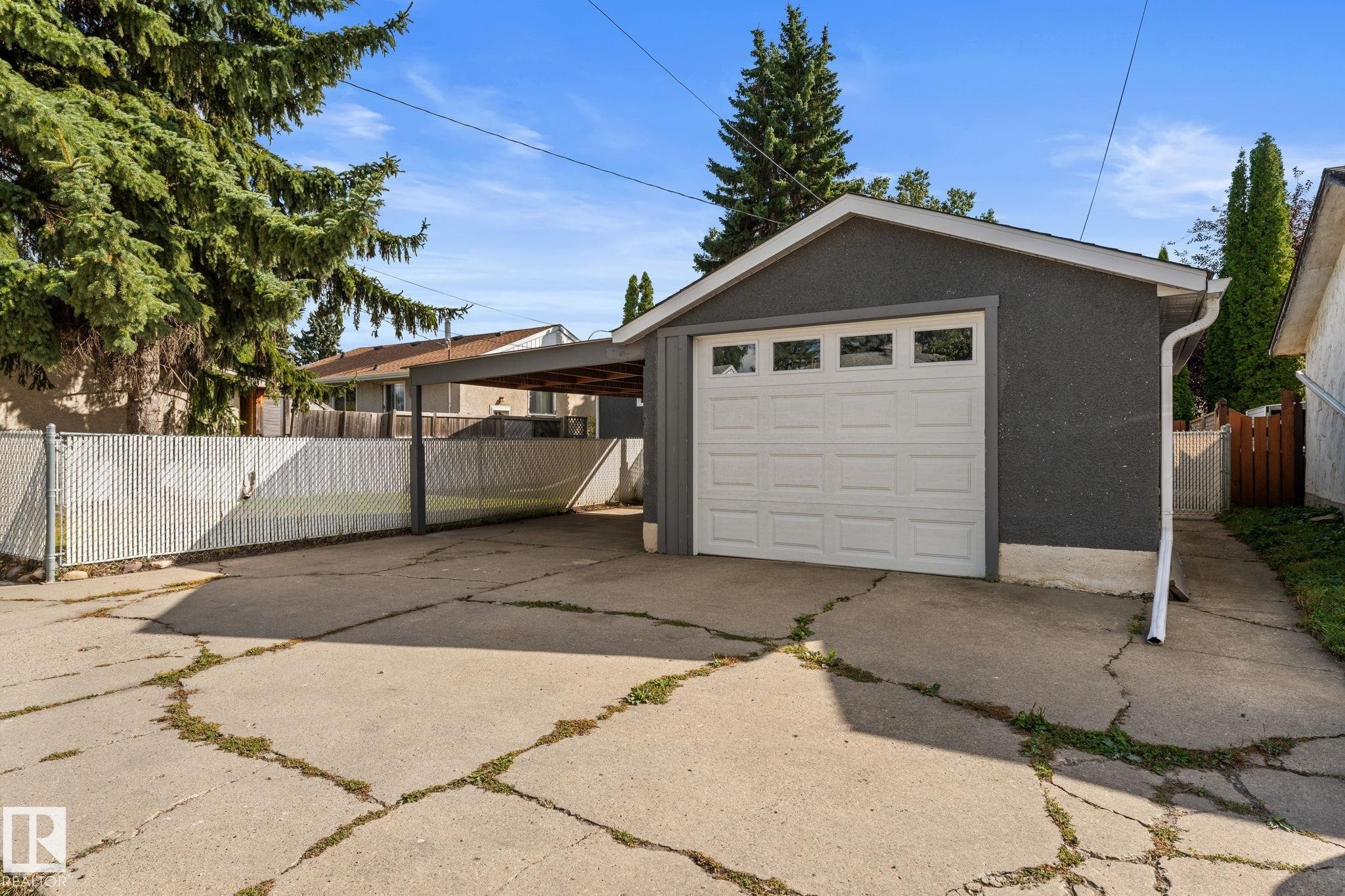 Detached single garage, single covered carport, concrete driveway, chain-link fencing, and mature trees - 6108 102 Avenue Nw, Edmonton, AB