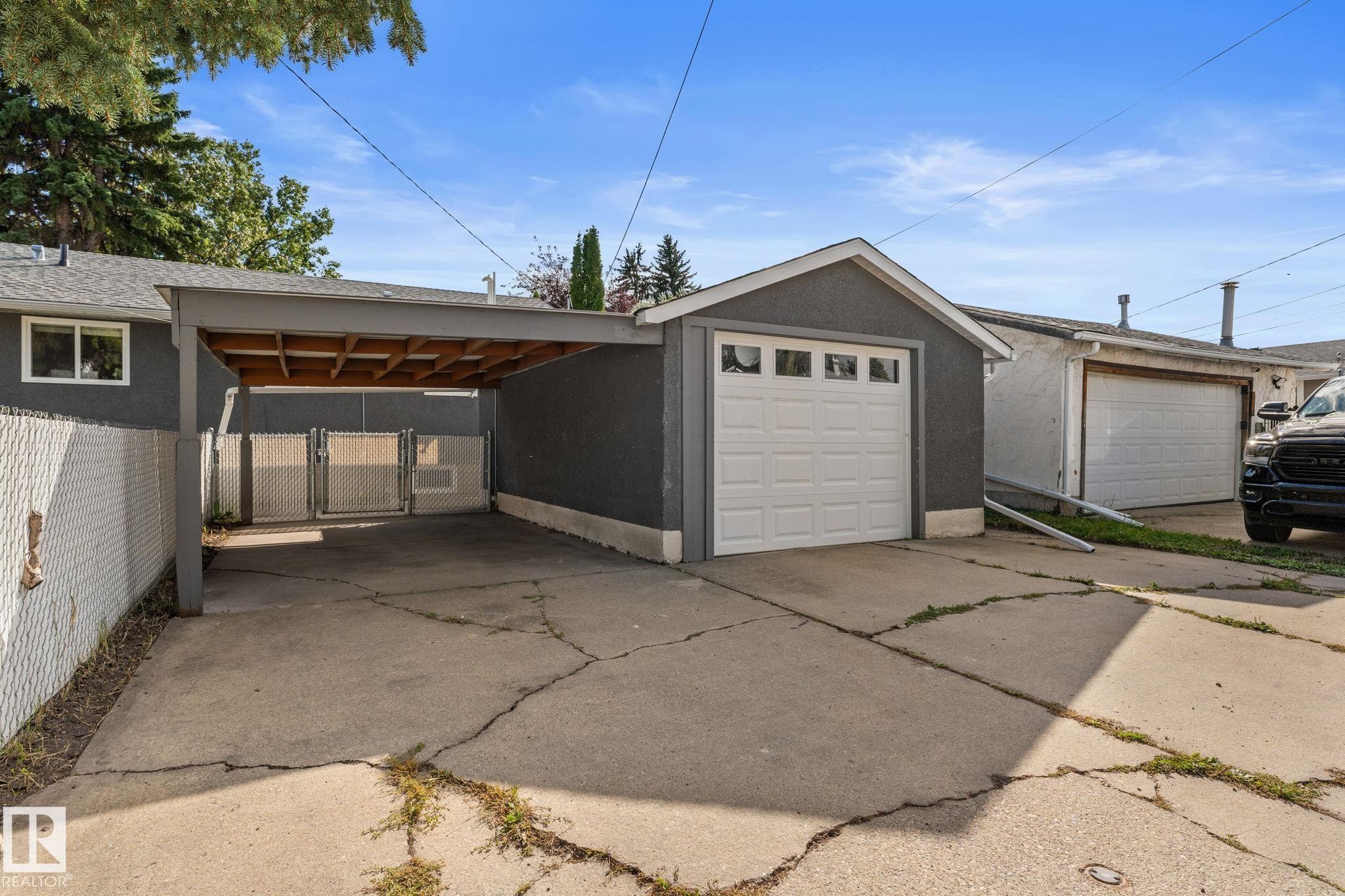 Detached single garage, single covered carport, concrete driveway, chain-link fencing, and mature trees - 6108 102 Avenue Nw, Edmonton, AB