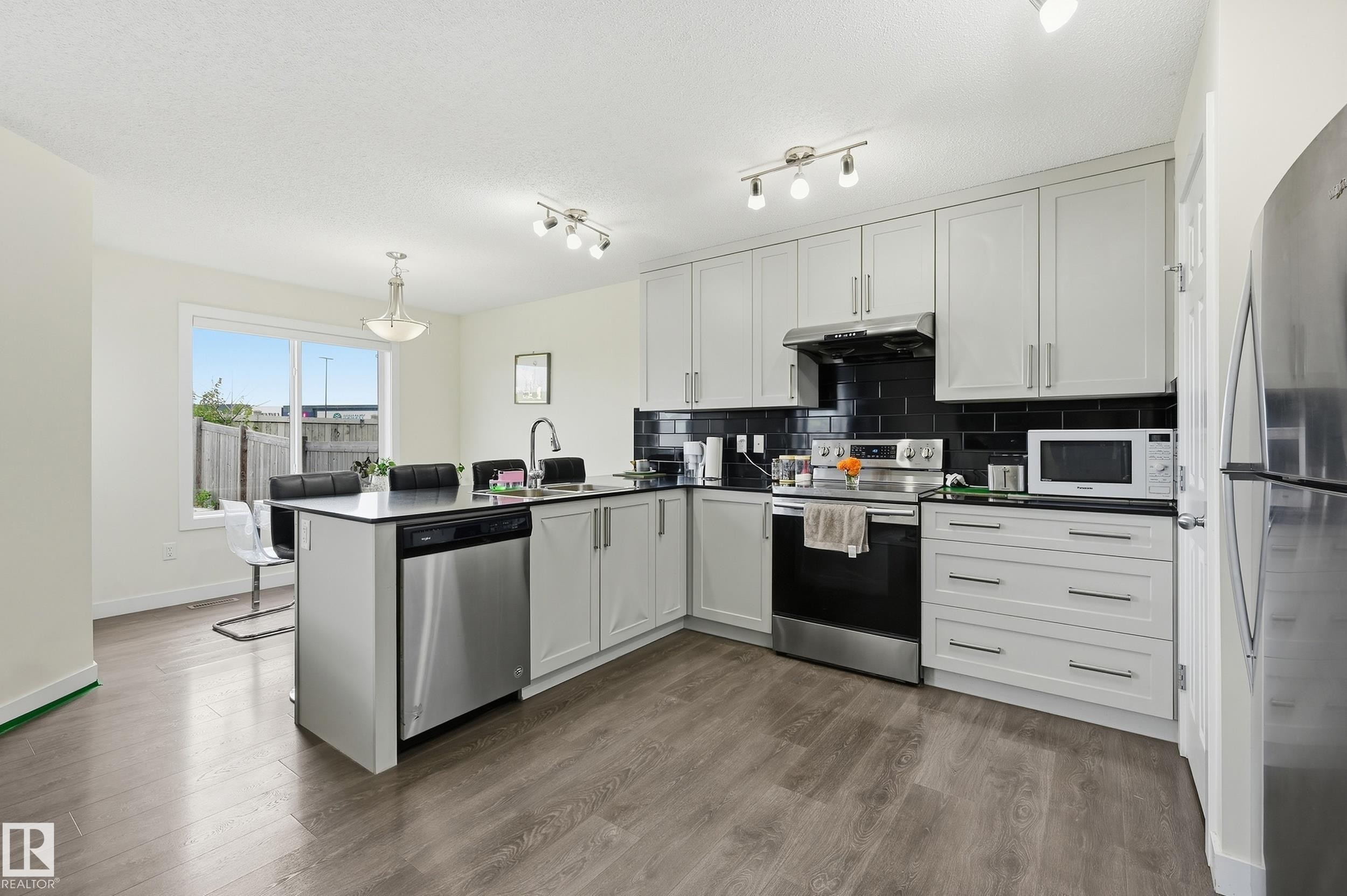 Modern kitchen featuring light gray cabinetry, black subway tile backsplash, stainless steel appliances, and wood-finish flooring - 941 Ebbers Crescent Nw, Edmonton, AB
