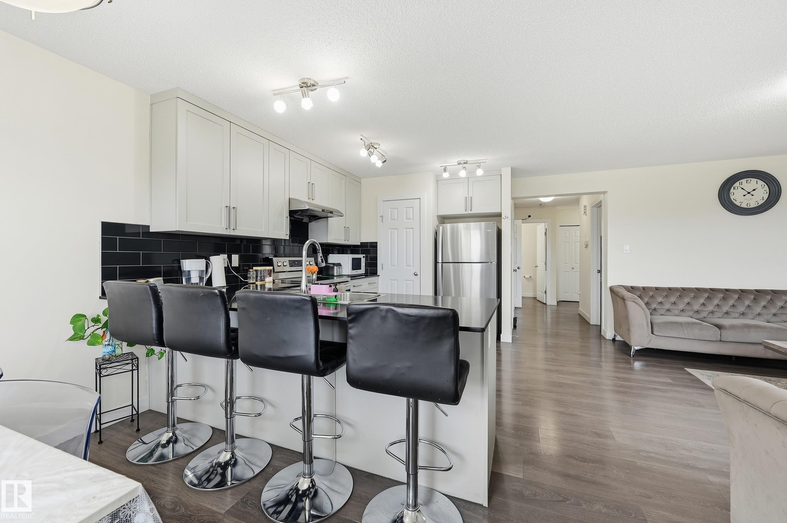 Kitchen featuring white cabinetry, black subway tile backsplash, stainless steel appliances, and a peninsula with seating - 941 Ebbers Crescent Nw, Edmonton, AB