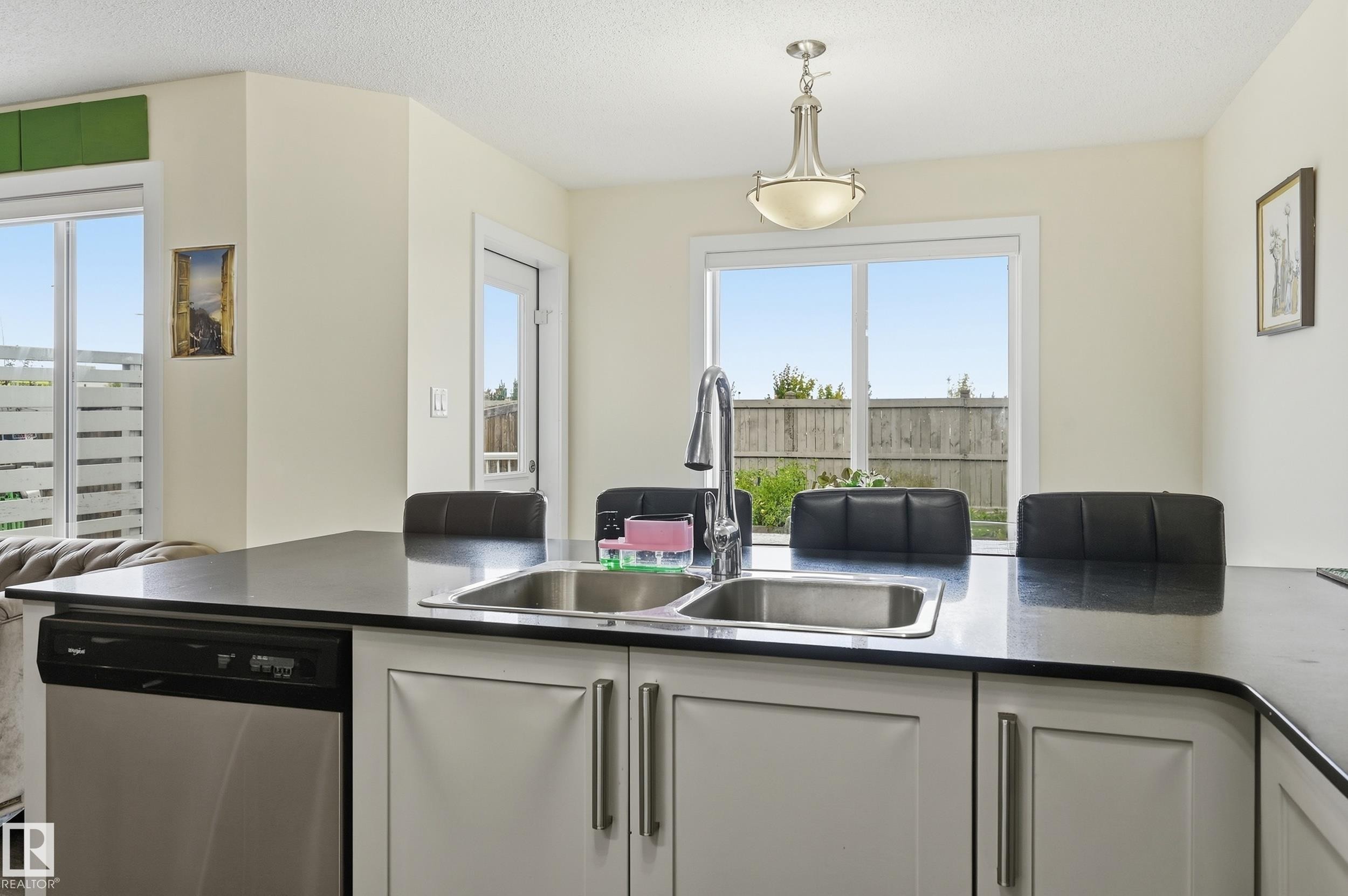 Central island with an undermount double basin sink, stainless steel dishwasher, and dark countertop - 941 Ebbers Crescent Nw, Edmonton, AB