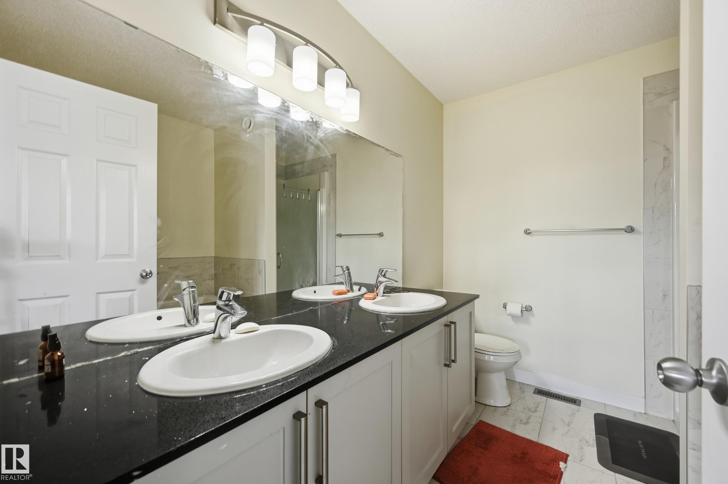 Dual basin vanity with a dark countertop and integrated sinks, illuminated by a contemporary light fixture - 941 Ebbers Crescent Nw, Edmonton, AB