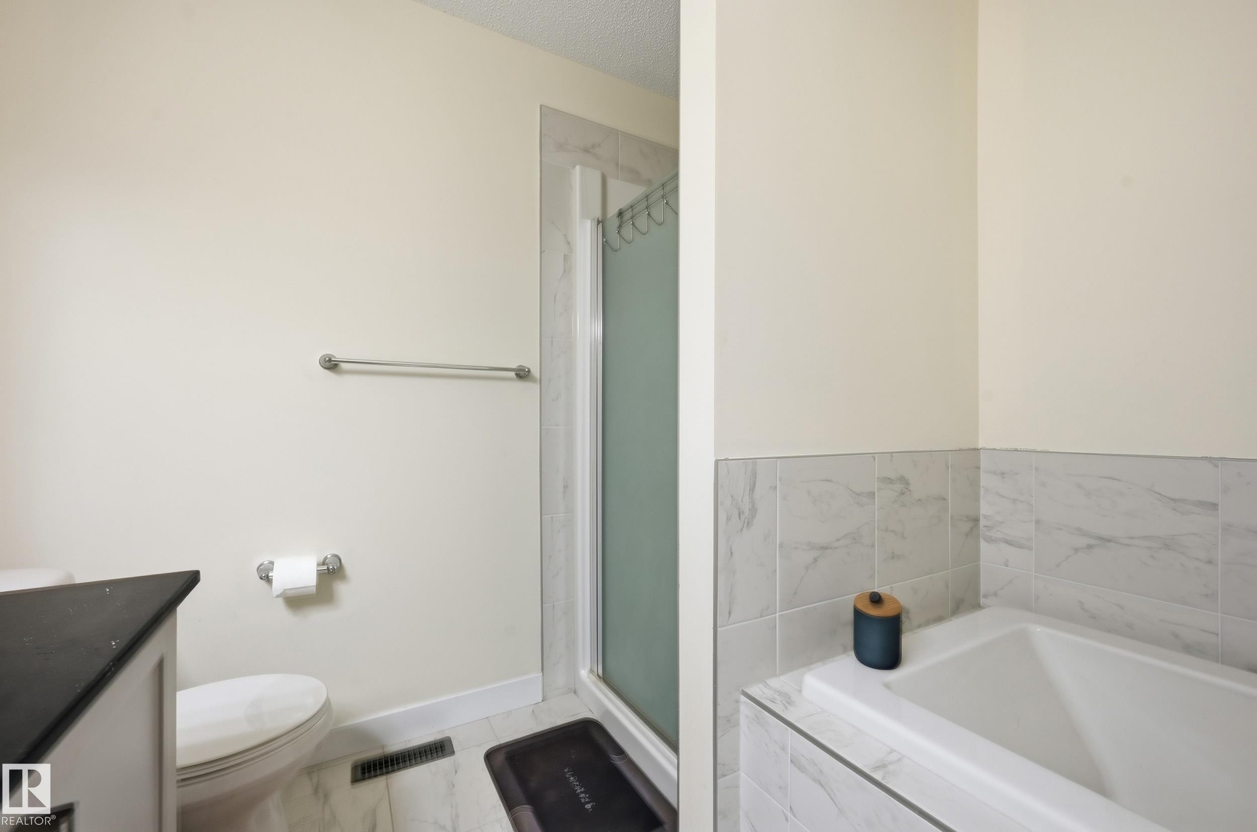Full-sized bathtub with tile surround, walk-in shower with frosted glass enclosure, and a vanity with a dark countertop - 941 Ebbers Crescent Nw, Edmonton, AB