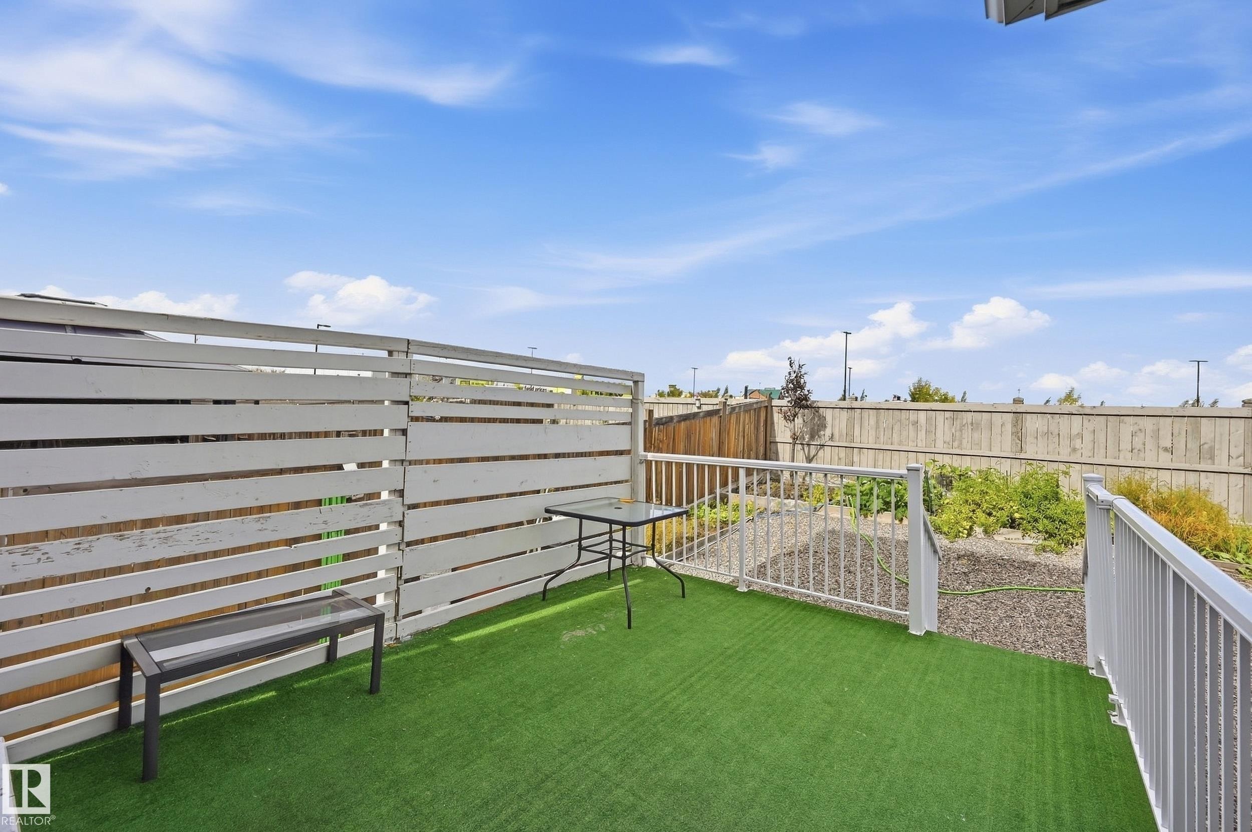 Outdoor patio featuring artificial turf, white horizontal slat fencing, white metal railing, and a sloped garden area - 941 Ebbers Crescent Nw, Edmonton, AB