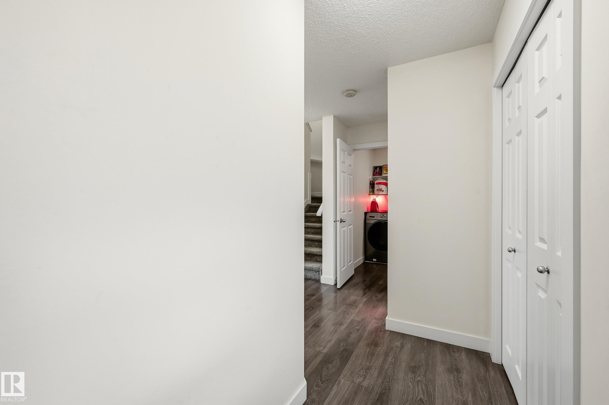 Wood-finish flooring with white baseboards, a bi-fold door closet, and a partial view of a laundry area - 941 Ebbers Crescent Nw, Edmonton, AB