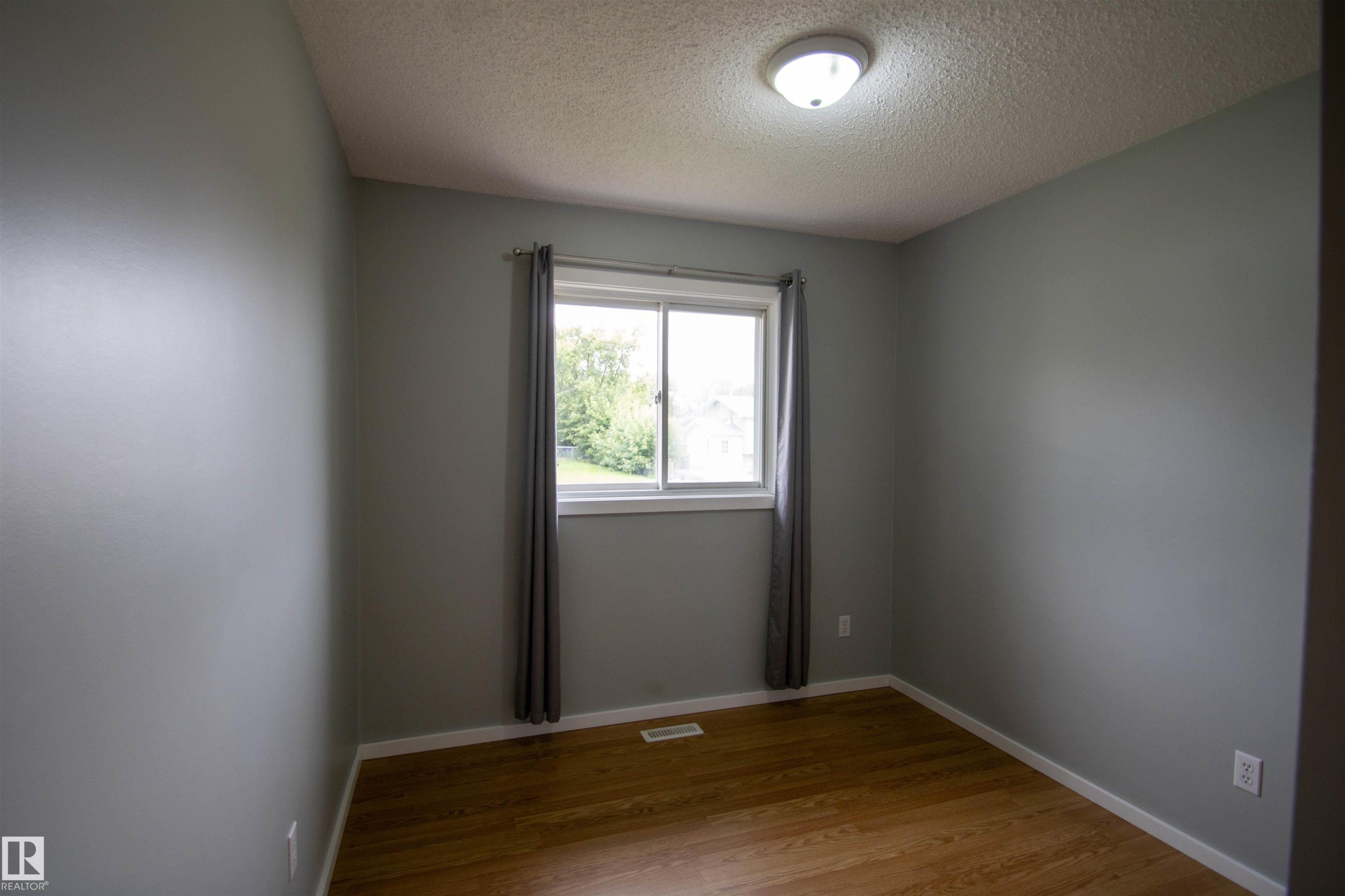 Bright room featuring wood-finish flooring, light gray walls, a white-framed window, and a flush-mount ceiling light - 4725 45 Ave, St. Paul Town, AB - Indoor Photo Showing Other Room
