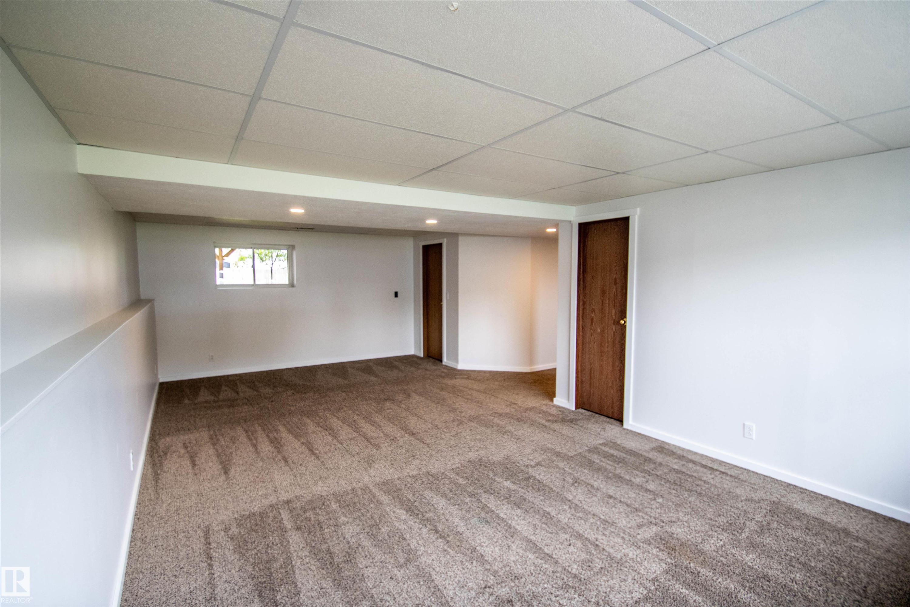 Spacious room featuring new carpeting, recessed lighting, white painted walls, a drop ceiling, and a visible window - 4725 45 Ave, St. Paul Town, AB - Indoor