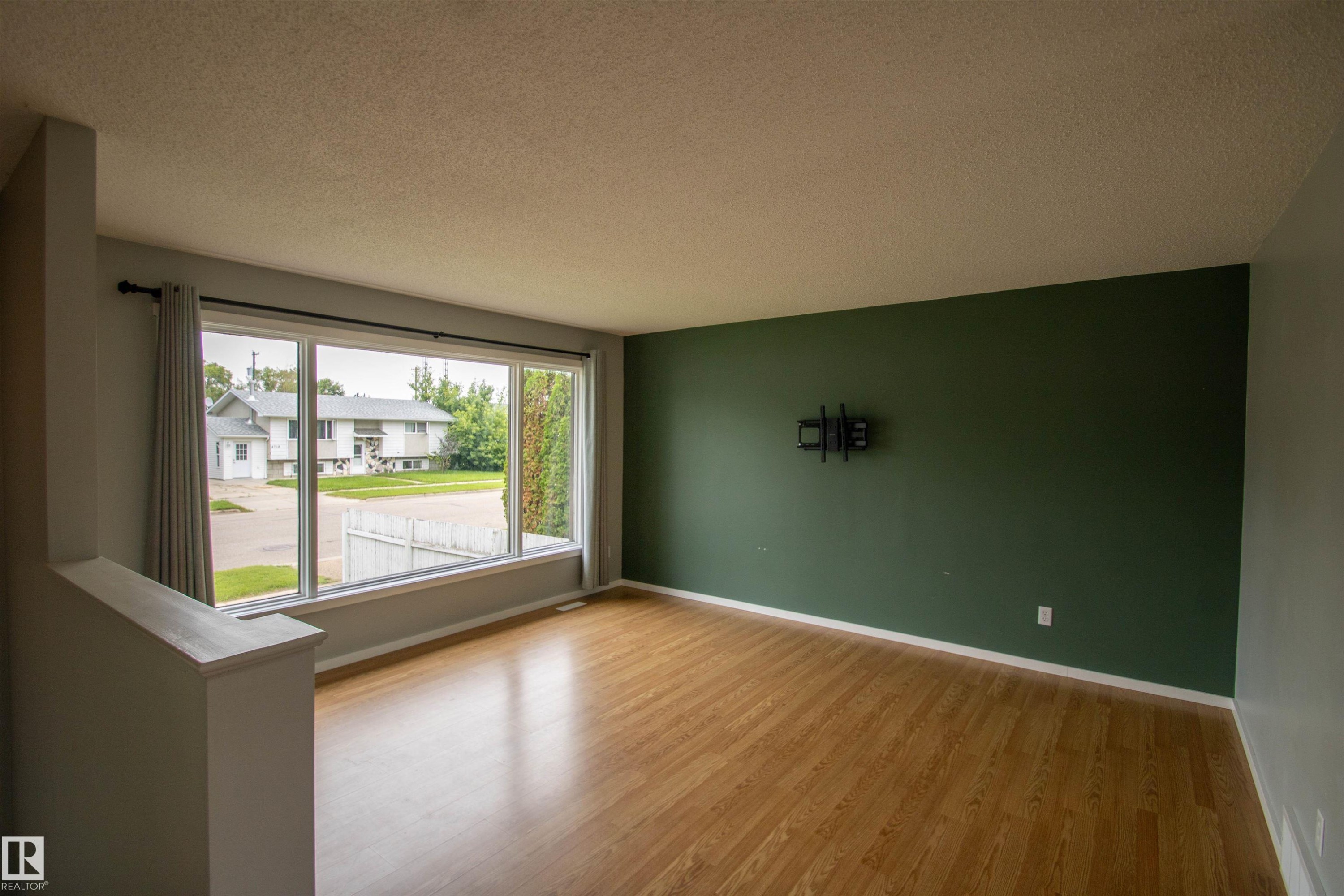 Spacious living area featuring expansive picture windows, wood-finish flooring, a contemporary dark green accent wall, and a textured ceiling - 4725 45 Ave, St. Paul Town, AB - Indoor Photo Showing Other Room