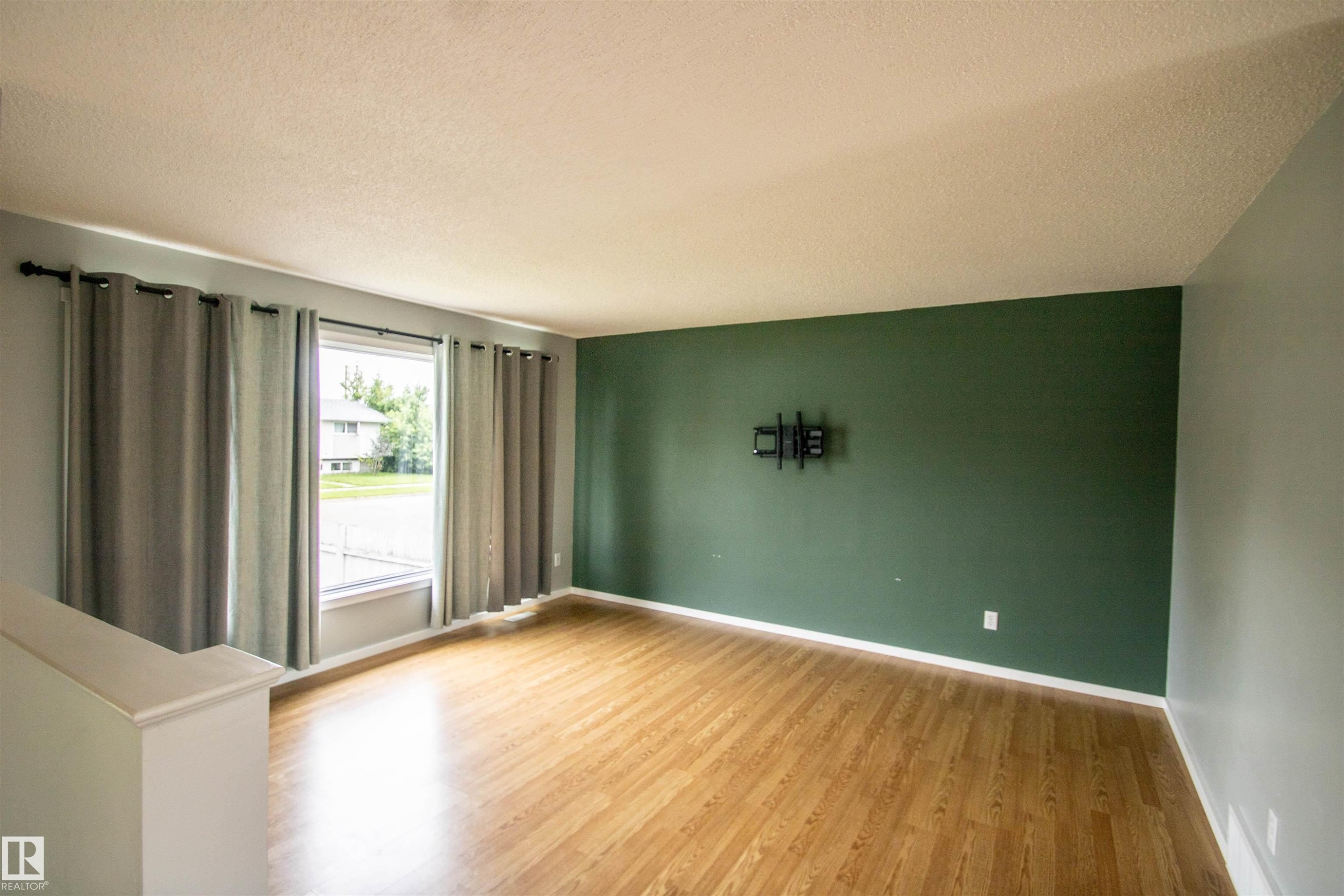 Open concept living area featuring wood-finish flooring, a prominent accent wall, and a large window with natural light - 4725 45 Ave, St. Paul Town, AB - Indoor Photo Showing Other Room