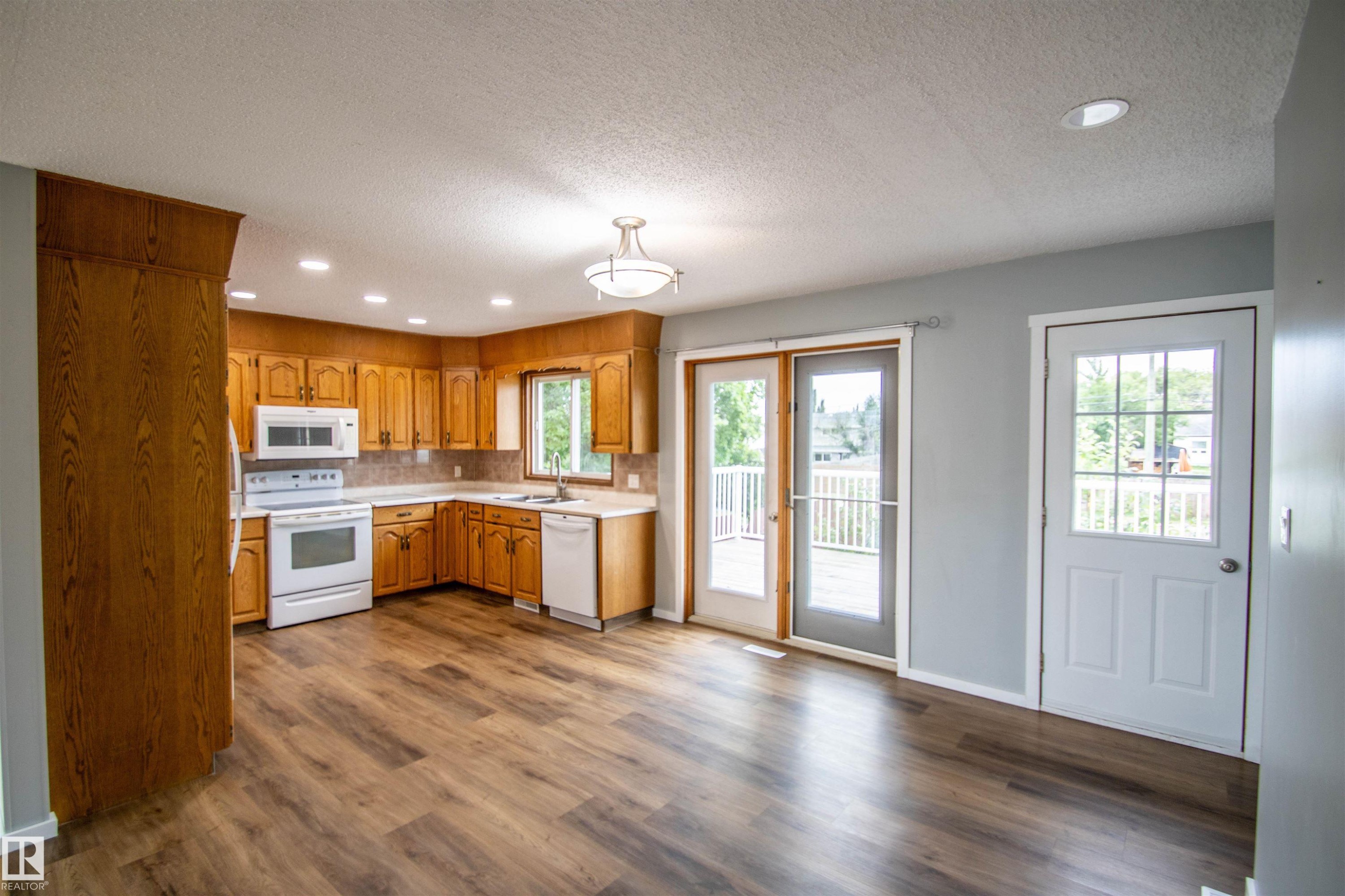Well-appointed kitchen featuring wood cabinetry, white appliances, and wood-finish flooring - 4725 45 Ave, St. Paul Town, AB - Indoor Photo Showing Kitchen