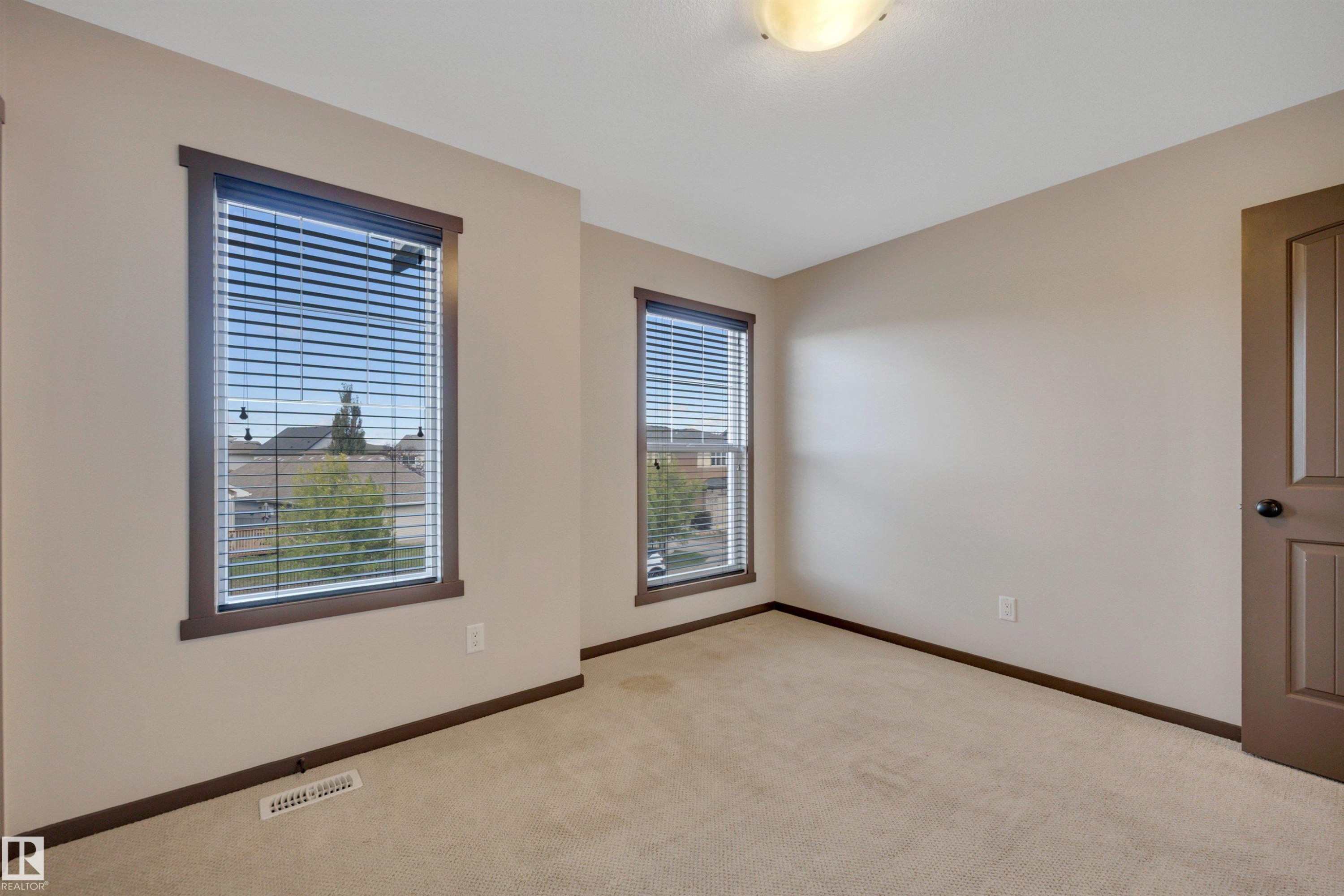 Plush carpeting, two windows with blinds, a modern ceiling light fixture, and a paneled interior door - 12903 205 Street Nw, Edmonton, AB