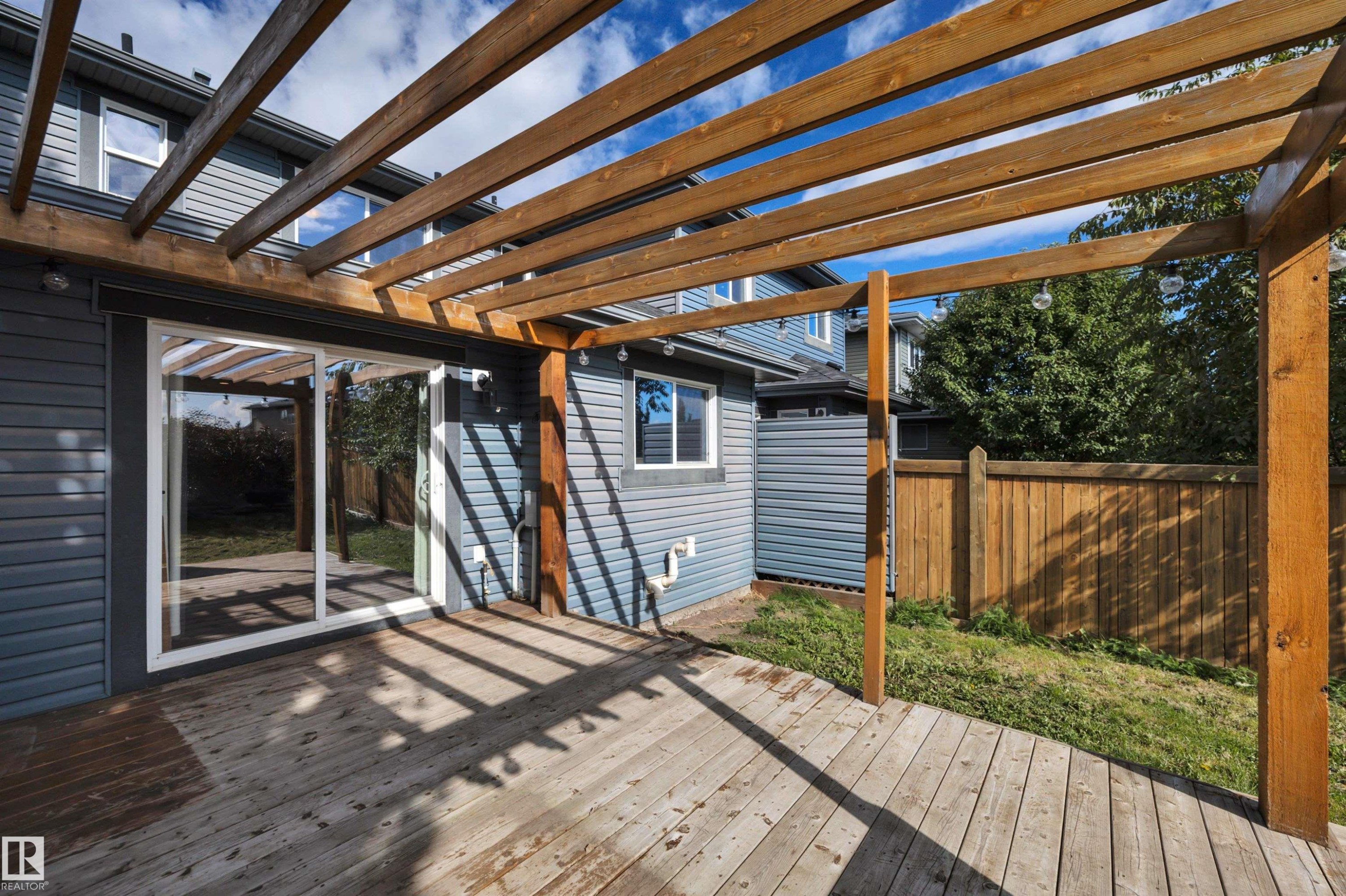 Expansive wood deck with a pergola, featuring a sliding glass door, durable siding, and a wooden privacy fence - 12903 205 Street Nw, Edmonton, AB